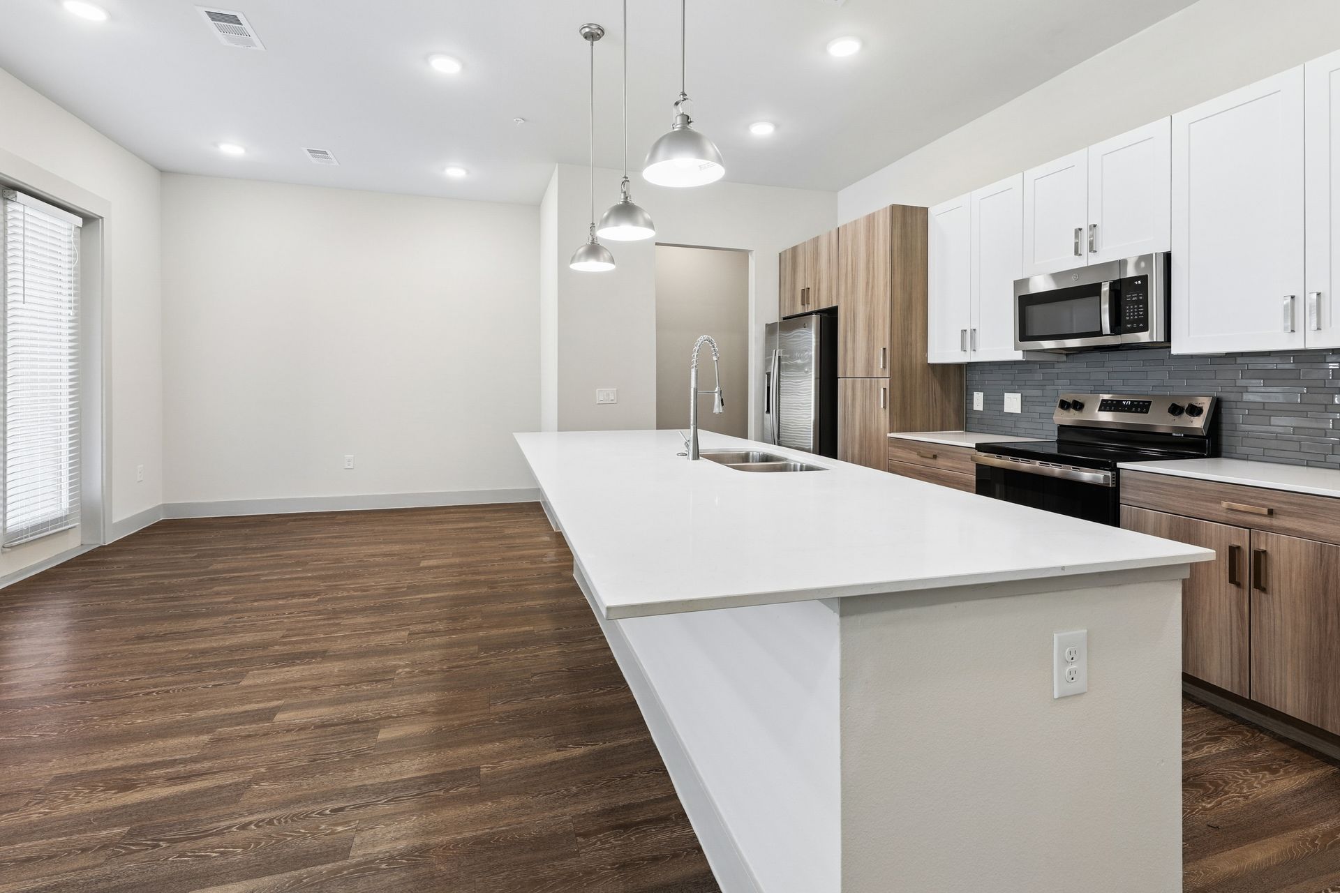 Modern open-plan kitchen with white cabinets, island, stainless appliances, and wood flooring