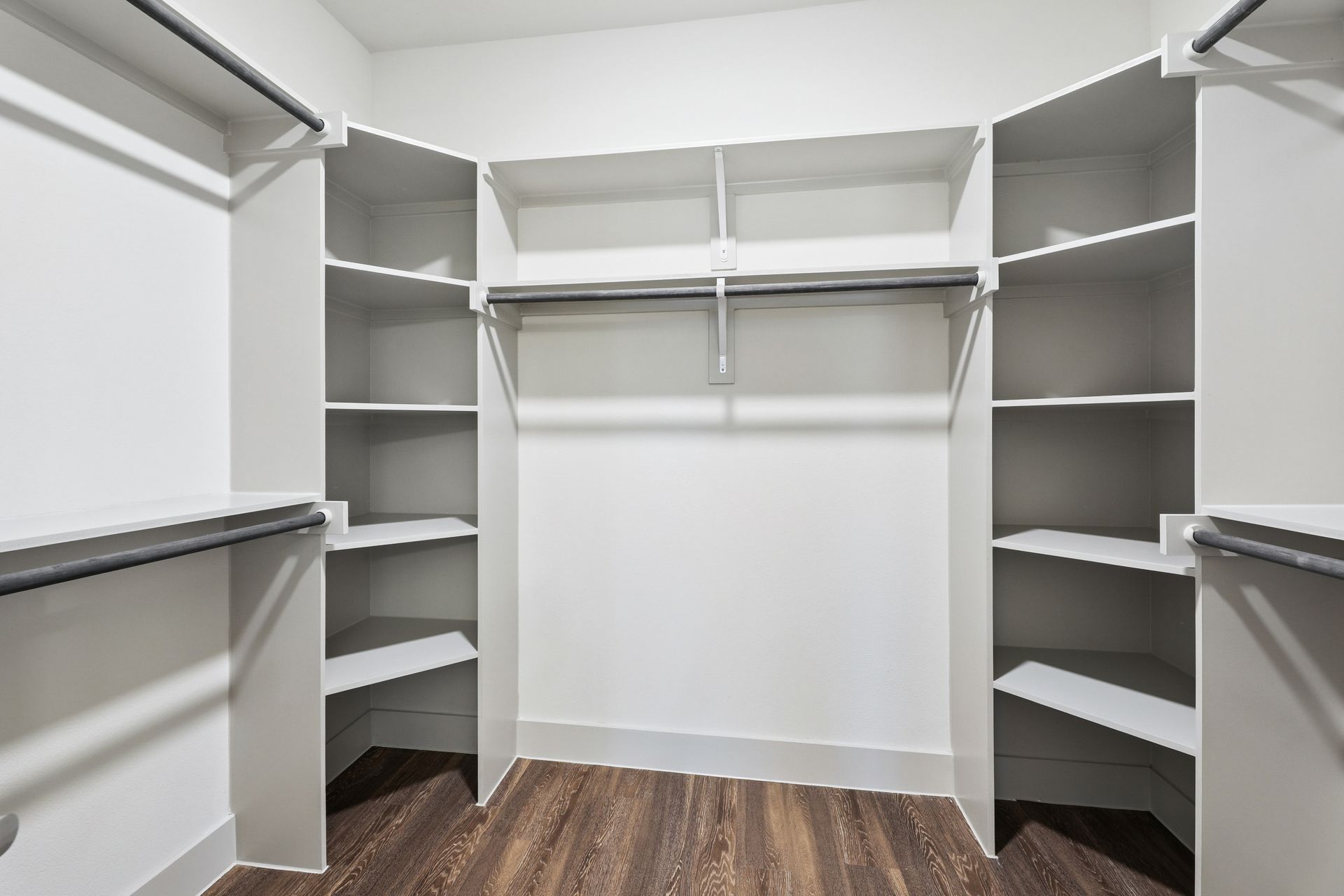 Walk-in closet with white shelves, hanging rods, and dark wood flooring