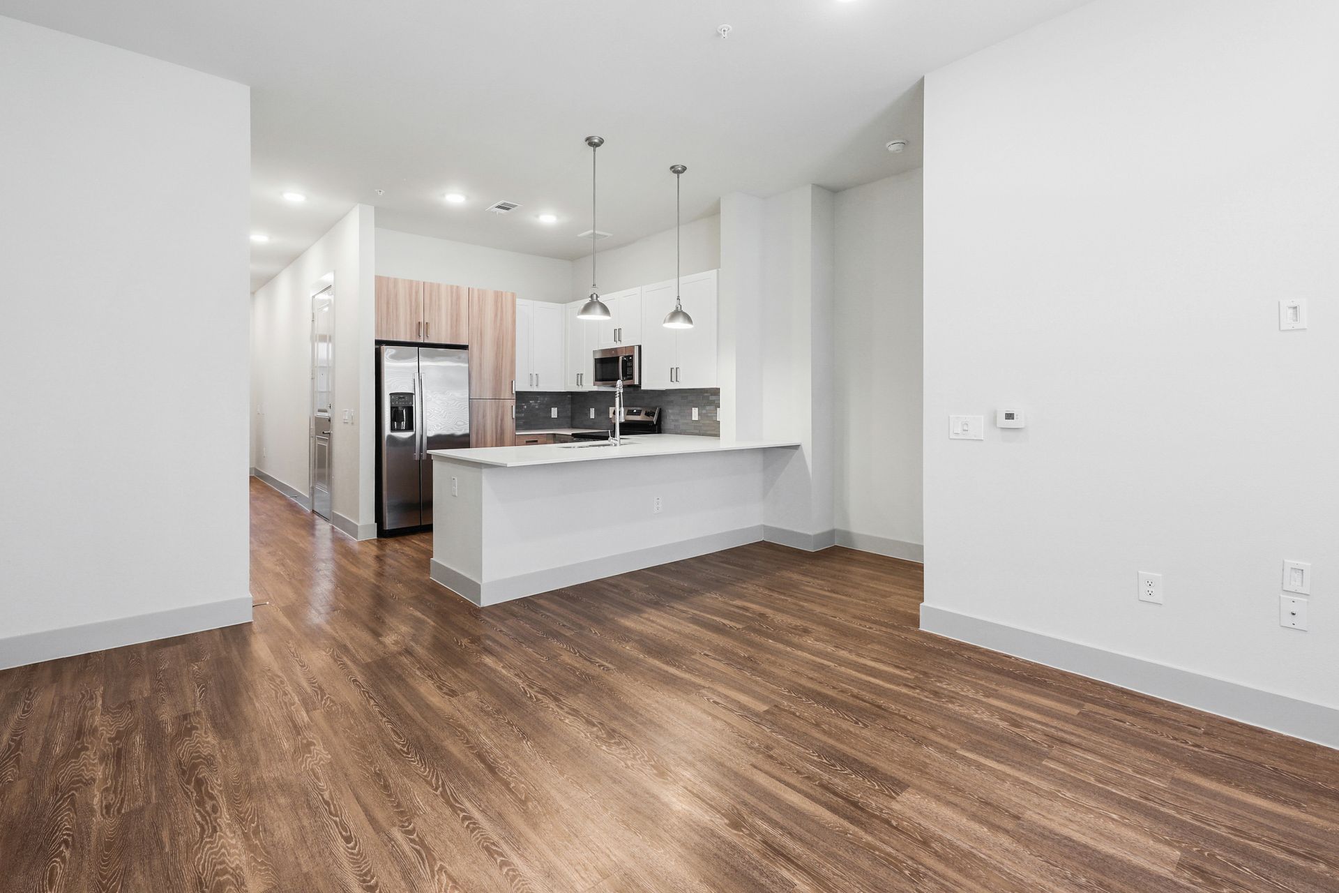 Empty modern kitchen and living area with wood floors and white walls