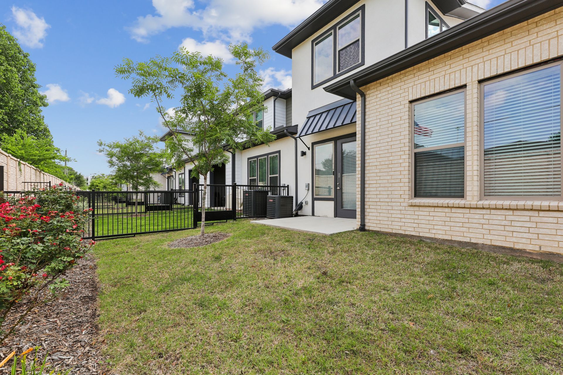 Townhouse exterior with small front lawn, black fence, and large windows under a blue sky