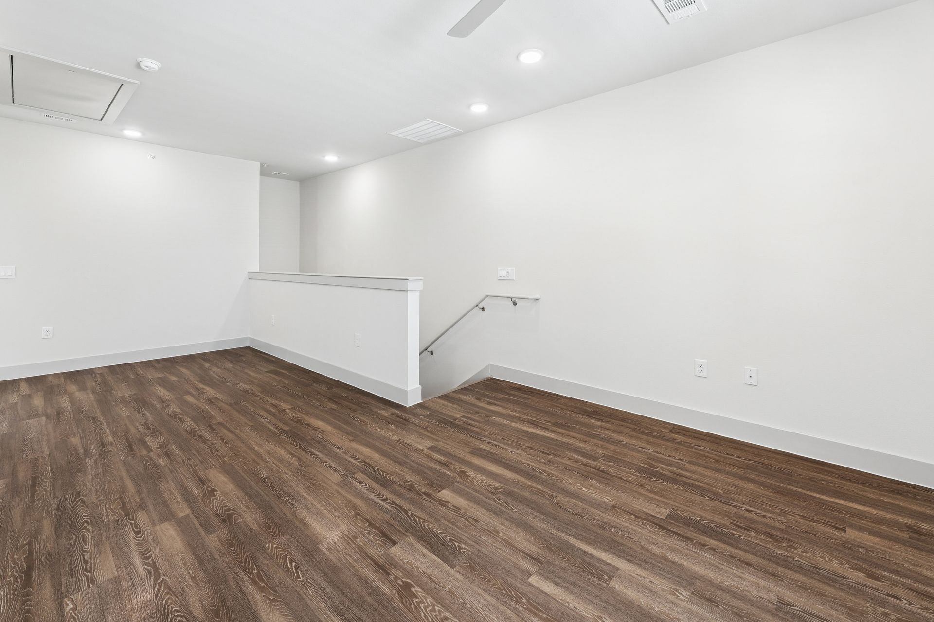 Empty white room with brown wood floors and a half wall staircase opening
