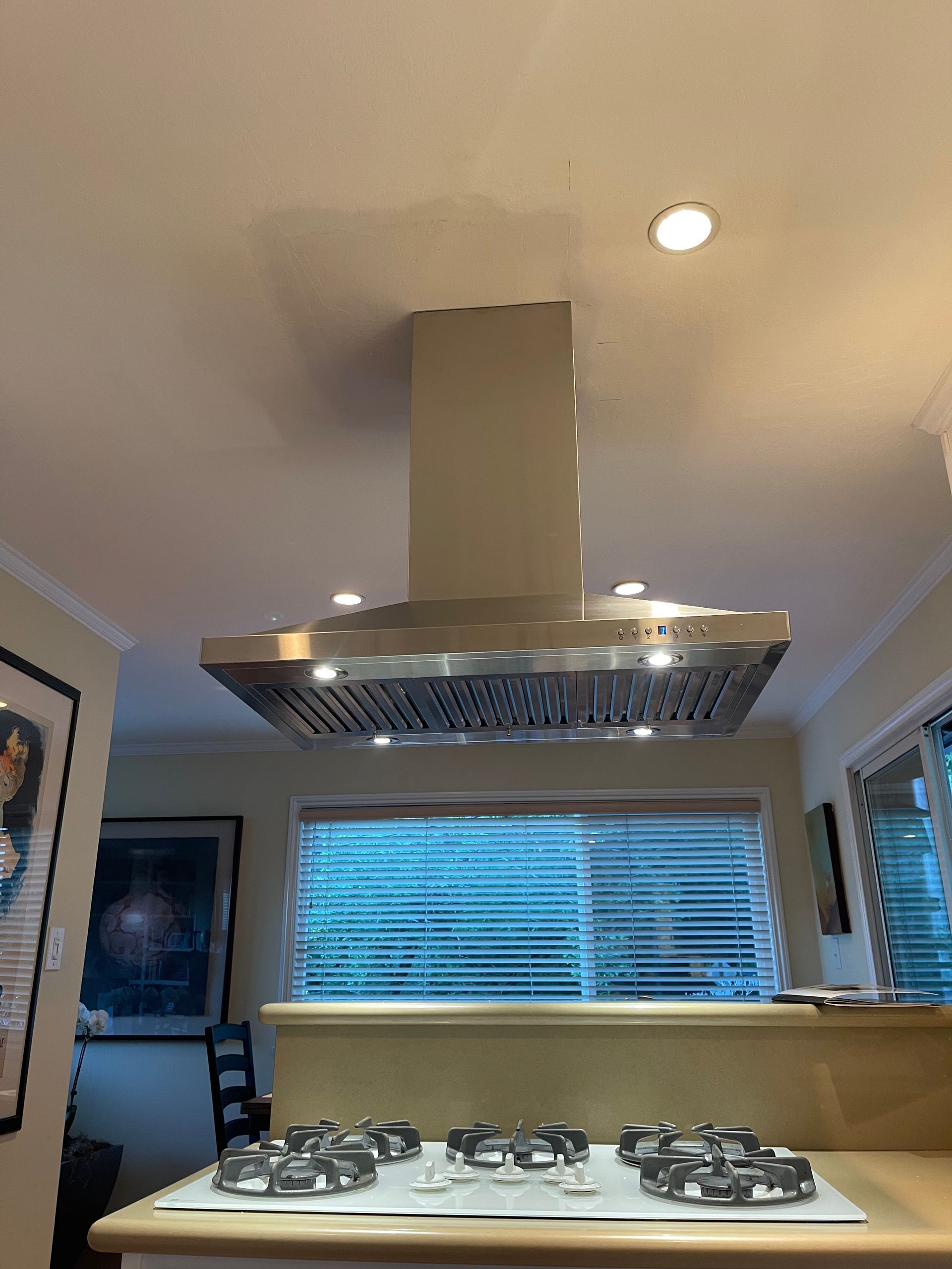 Range hood above a gas stovetop in a kitchen with a window and a light fixture.