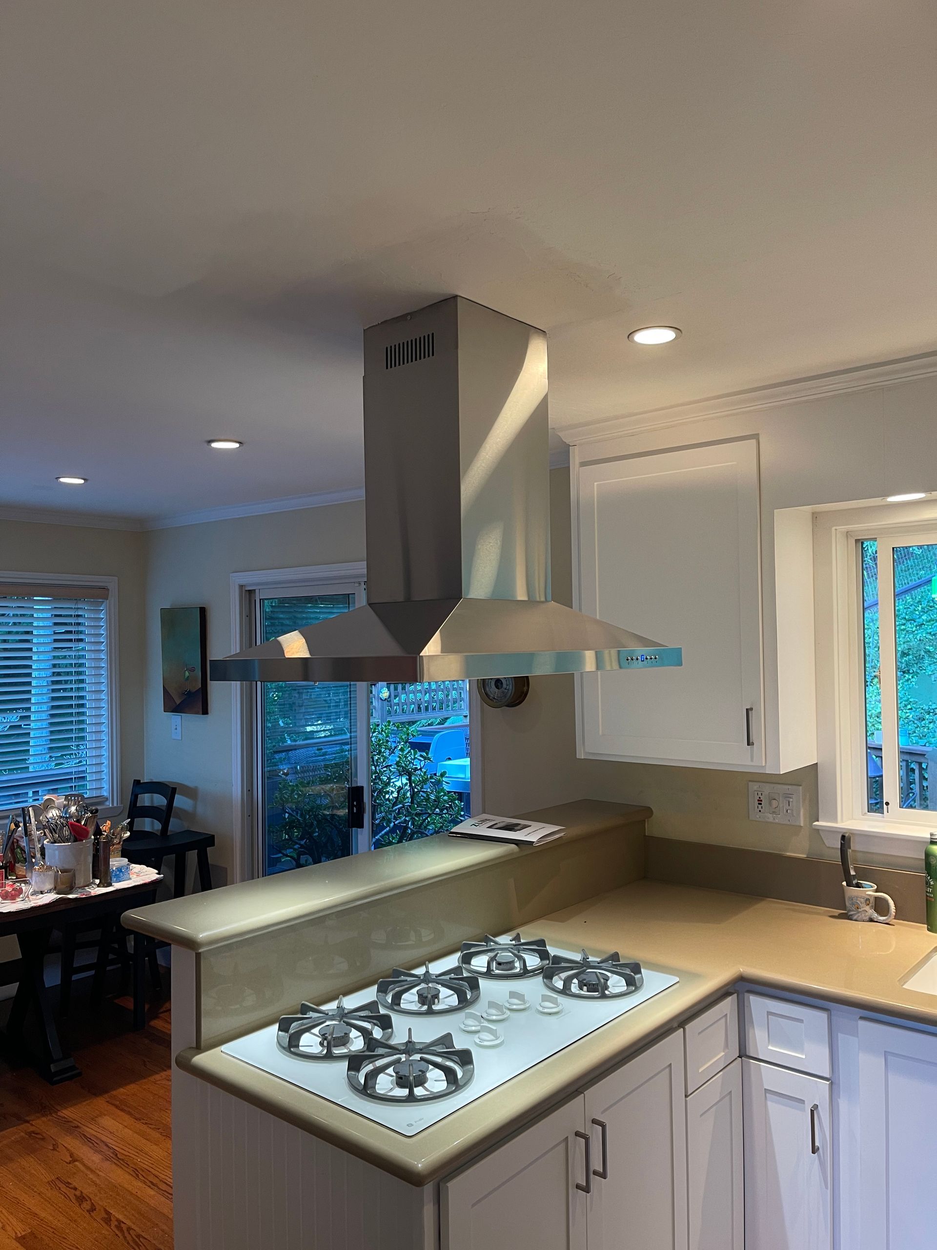 Kitchen with stove, exhaust hood, and countertop. White cabinets and beige countertop.