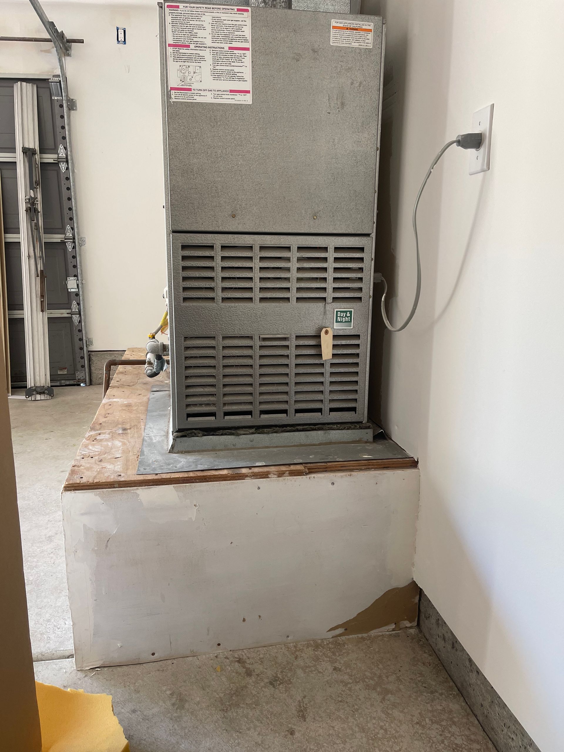 HVAC unit on a raised platform in a garage, next to a wall.
