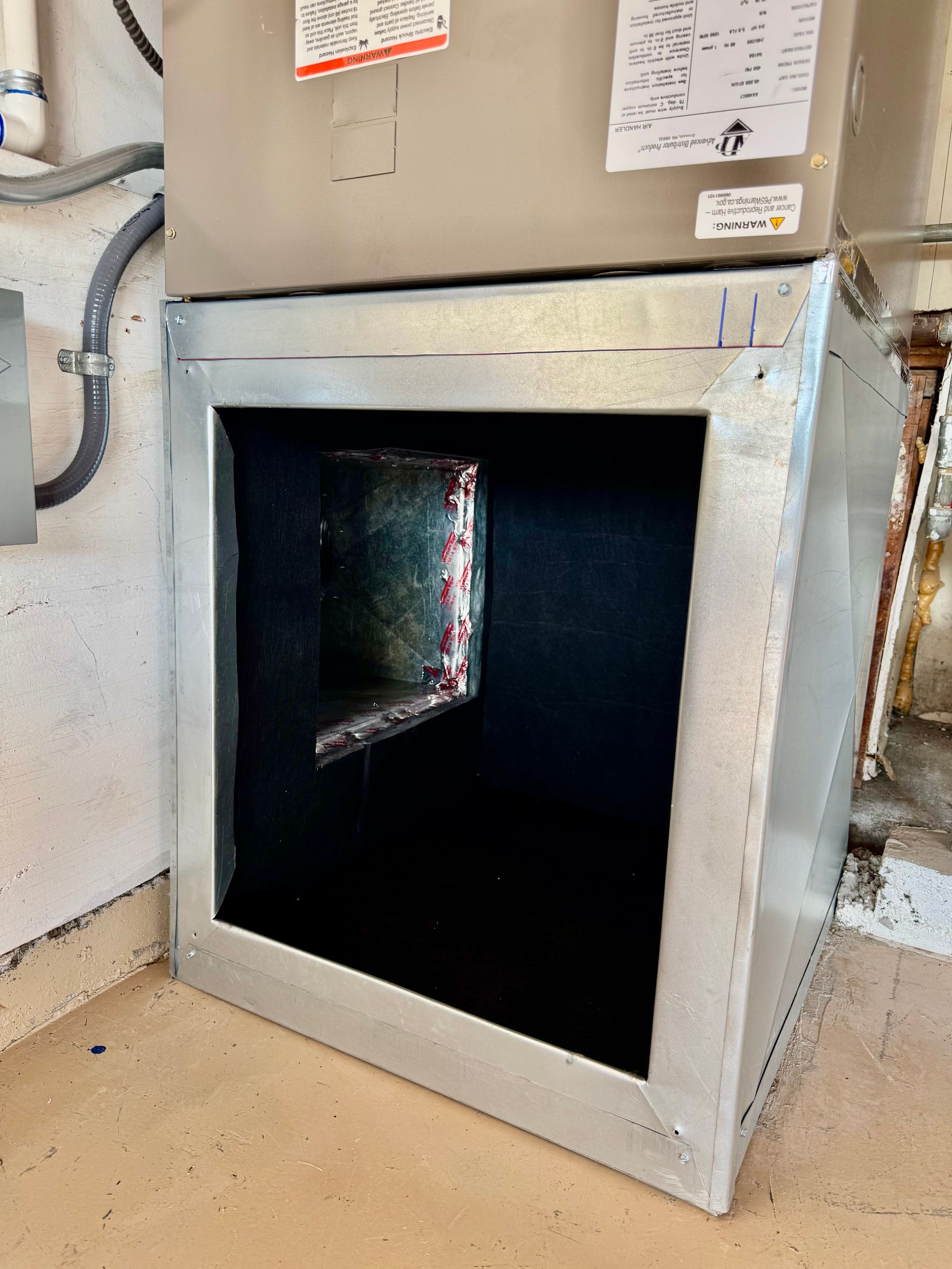 Silver HVAC unit with open filter compartment, black filter, concrete floor.
