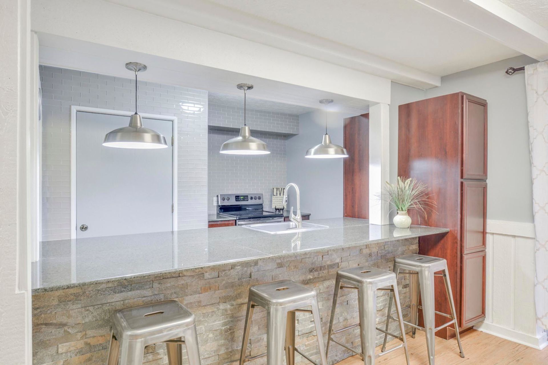 clubhouse kitchen with granite island, three pendant lights, and bar stools in a bright open layout