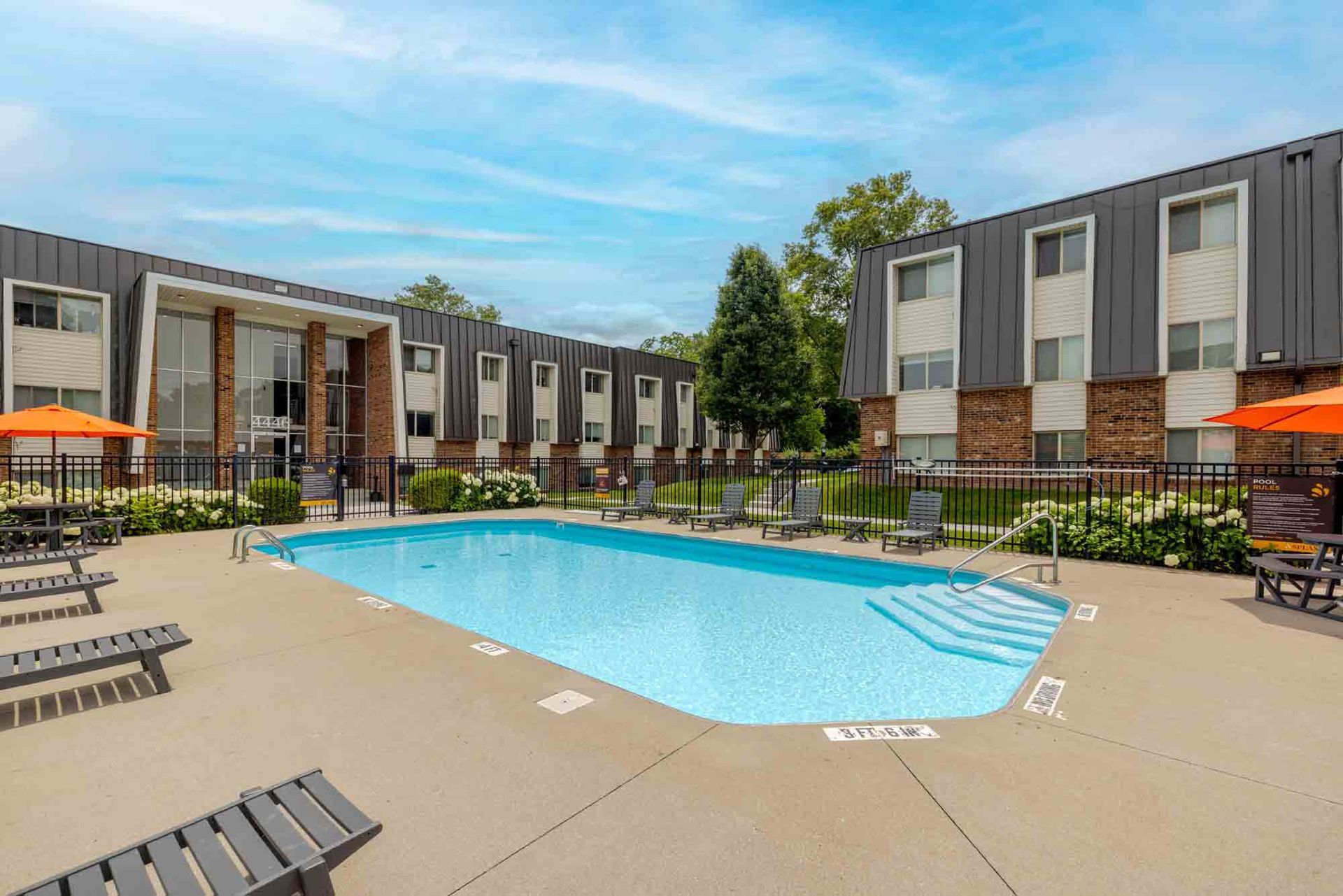 Apartment courtyard with a turquoise pool, tan deck chairs, and gray two-story buildings around it