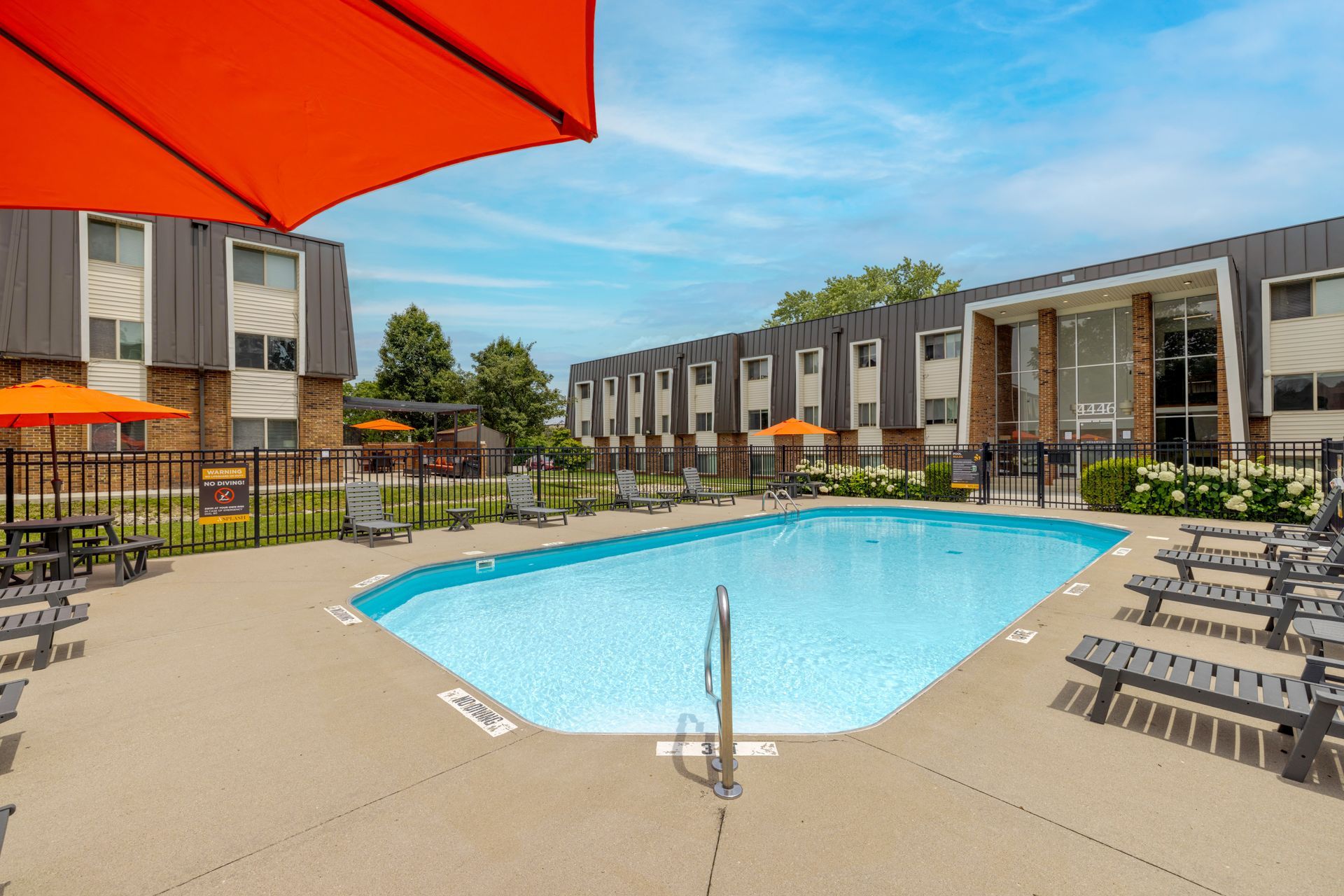 Courtyard swimming pool with blue water, lounge chairs, and apartment buildings under a red umbrella.