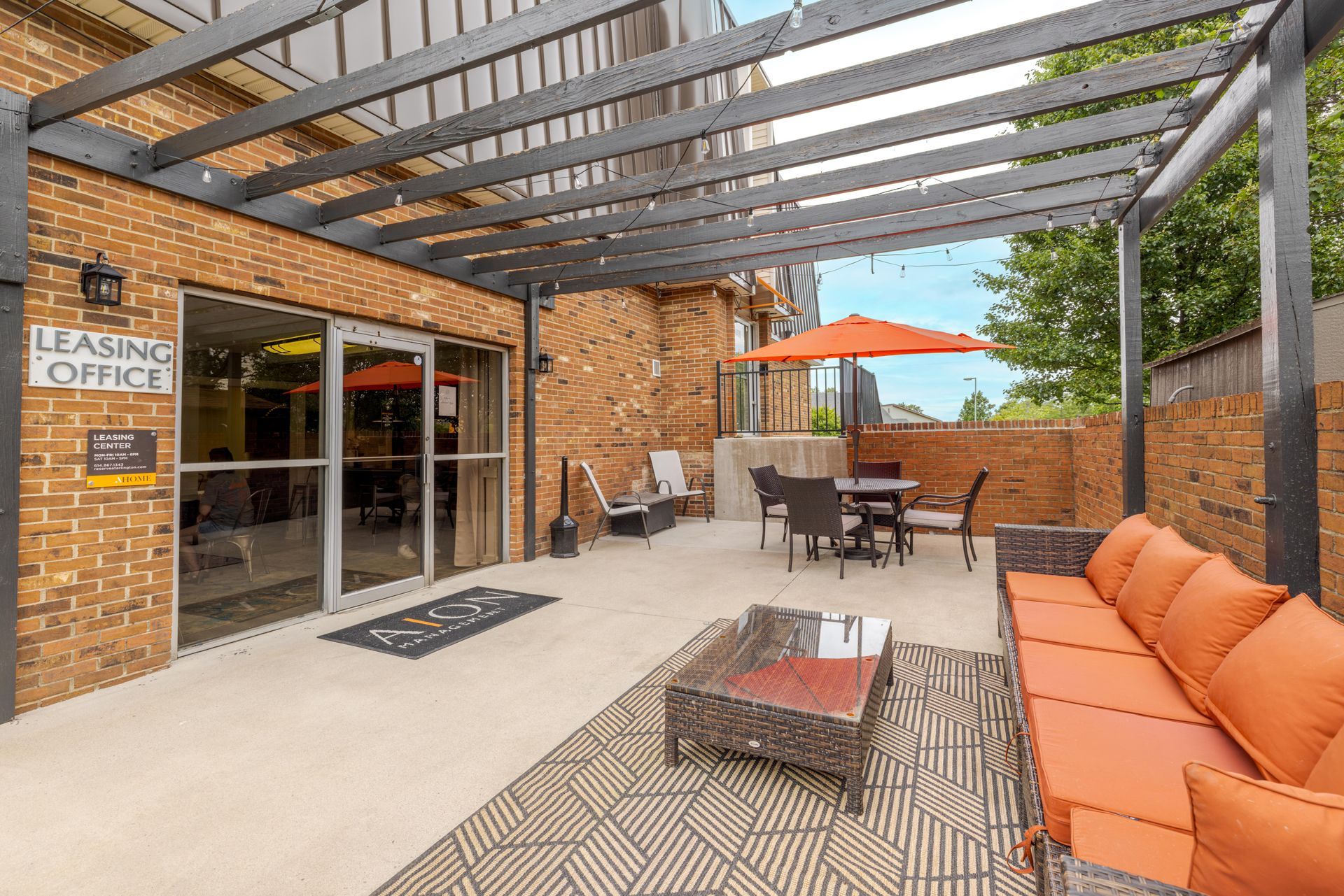 Covered outdoor patio with orange cushions, table, chairs, and glass doors beside a leasing office