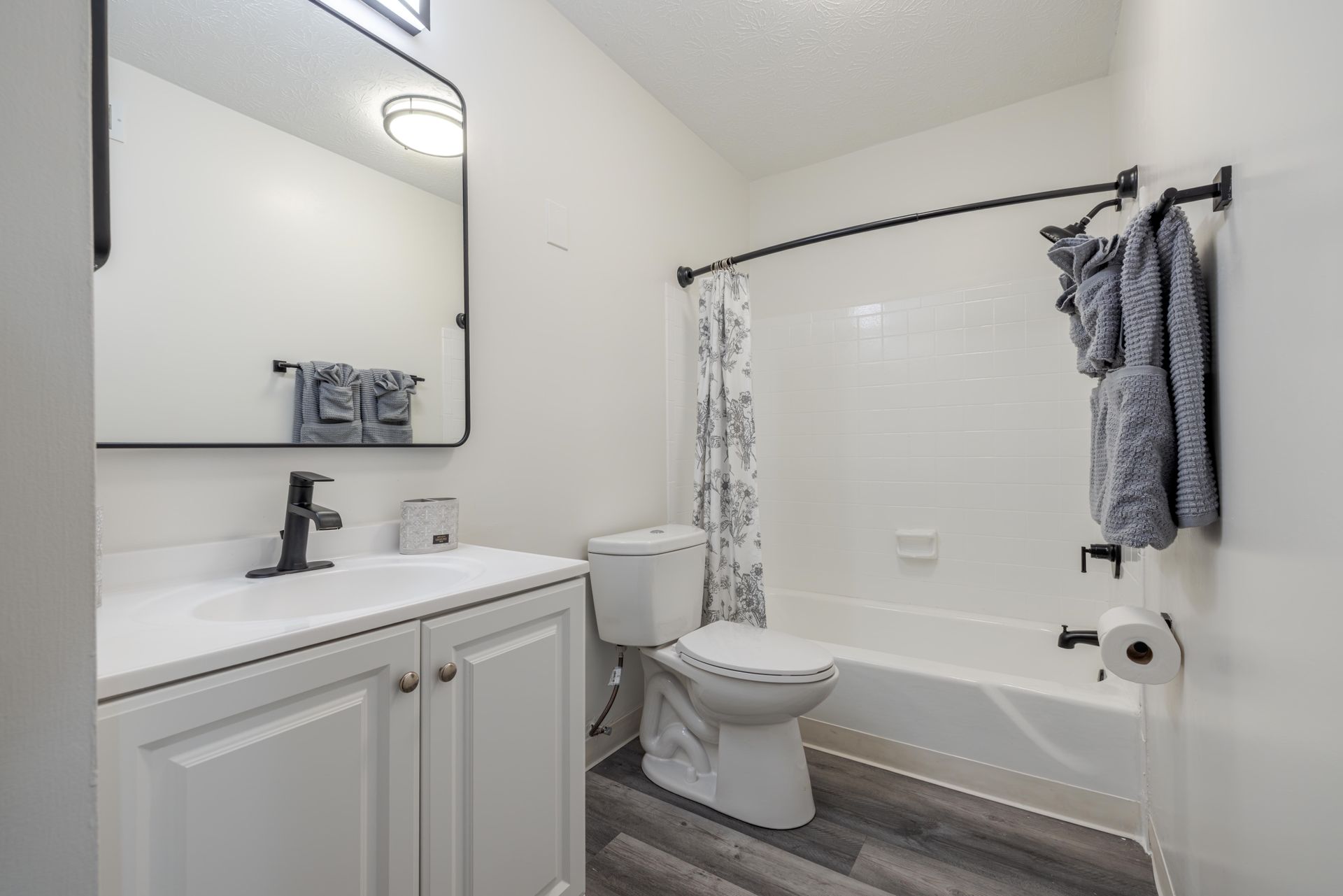 White bathroom with vanity, mirror, toilet, and tub with gray shower curtain and towels at the Reserves at Arlington in Columbus, OH.