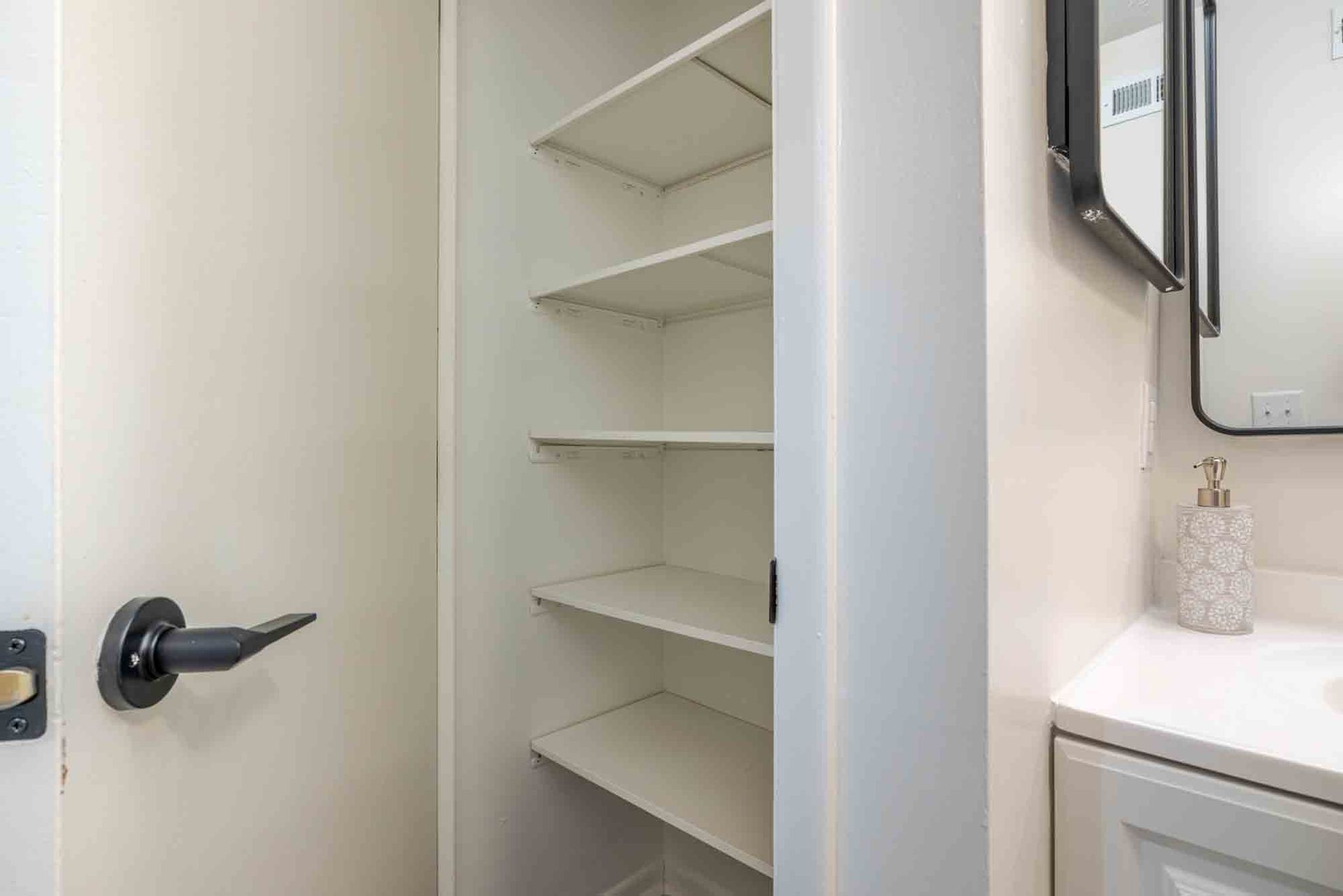 Open linen closet with white shelves beside a bathroom vanity and mirror. at the Reserves at Arlington in Columbus, OH.