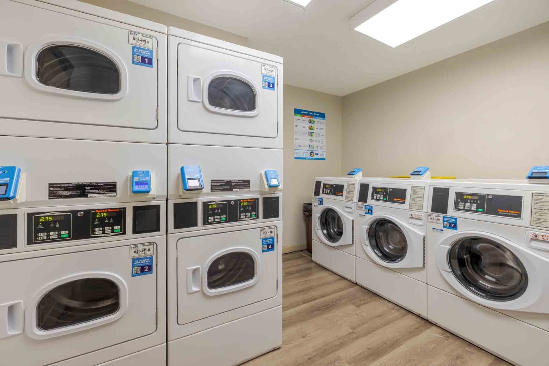 Bright shared laundry room with stacked washers and dryers along beige walls and wood-look flooring
