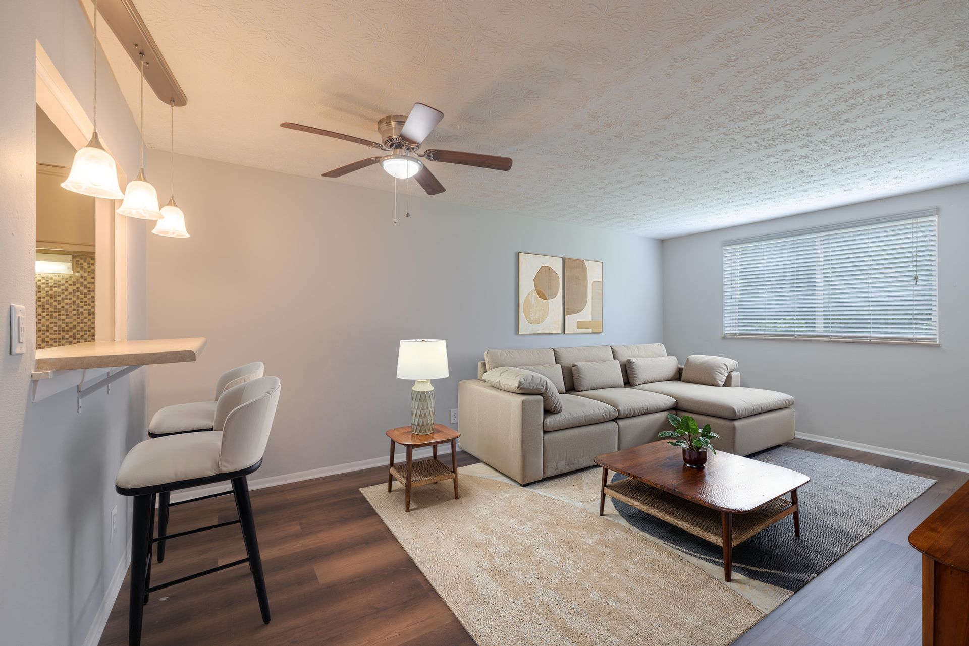 Modern living room with gray sectional, coffee table, rug, lamps, and ceiling fan; kitchen bar nearby at the Reserves at Arlington in Columbus, OH.