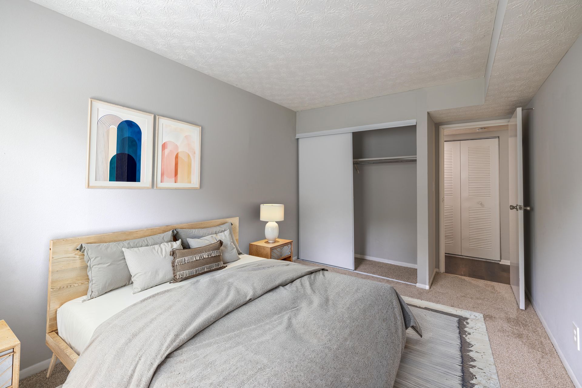 Bright bedroom with a bed, wall art, open closet, and carpeted floor at the Reserves at Arlington in Columbus, OH.