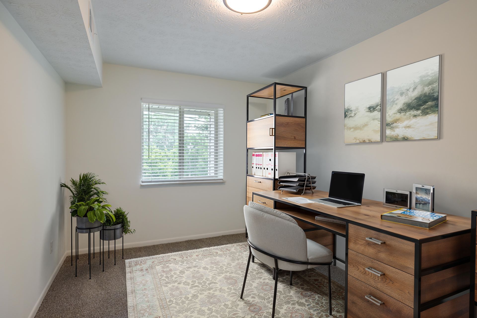 bedroom staged as home office with wood desk, computer, chair, plant, window, and wall art. at the Reserves at Arlington in Columbus, OH.
