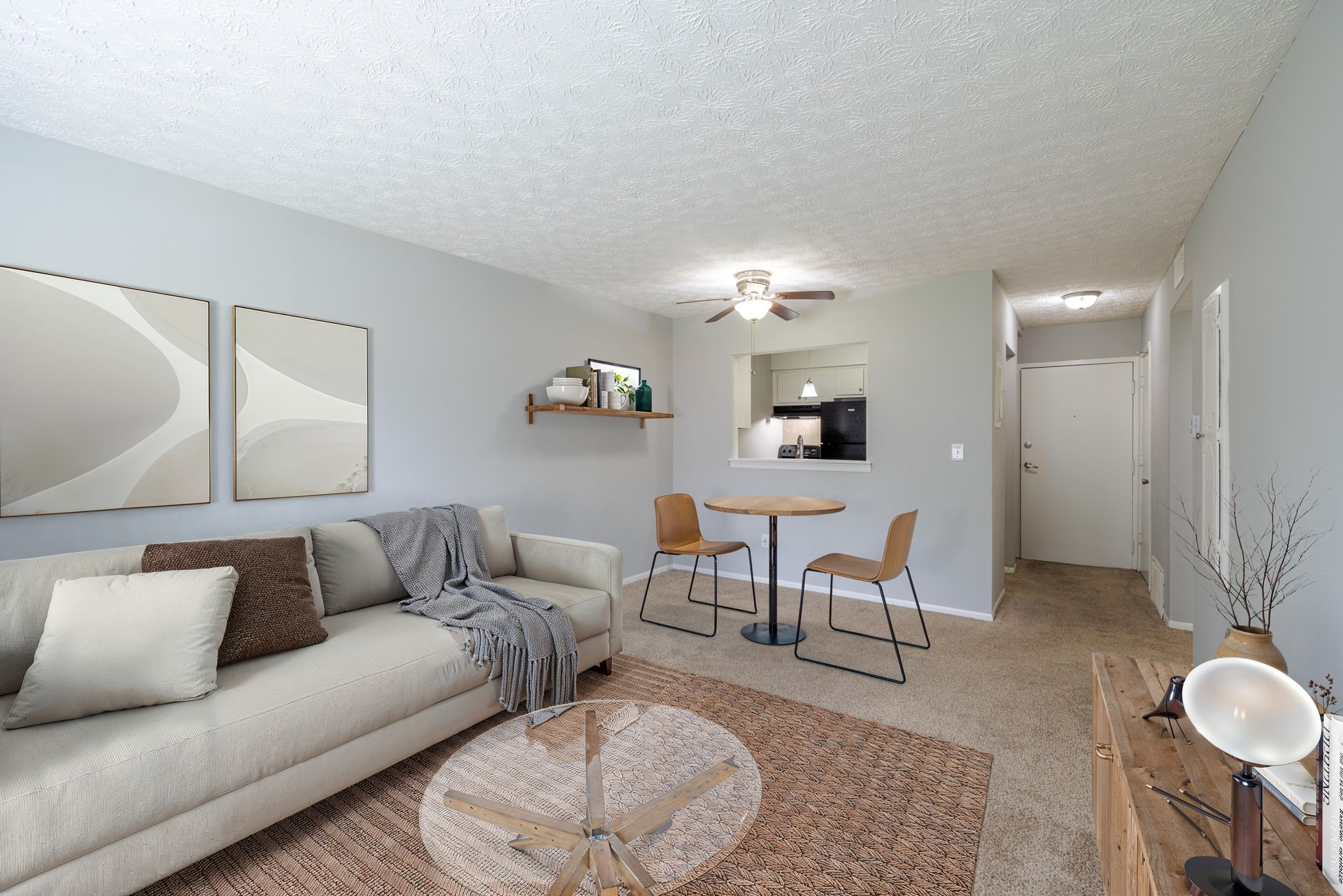 Bright living room with gray sofa, dining nook, beige carpet, and wall art. at the Reserves at Arlington in Columbus, OH.