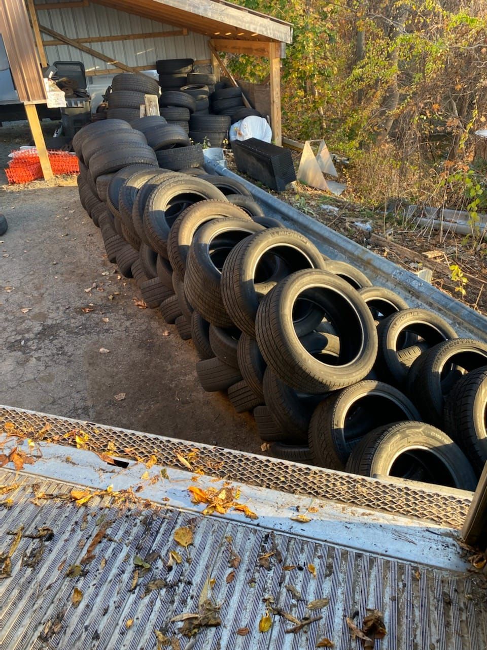 A large stack of black tires, some arranged in rows, outdoors near a wooden structure.