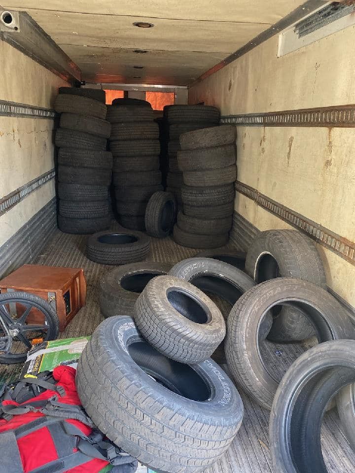 Inside a truck, many tires are stacked and scattered. A red bag and box are also present.