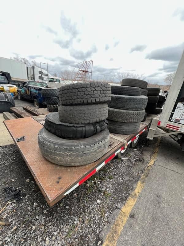 Stack of used tires on a flatbed trailer in a junkyard.