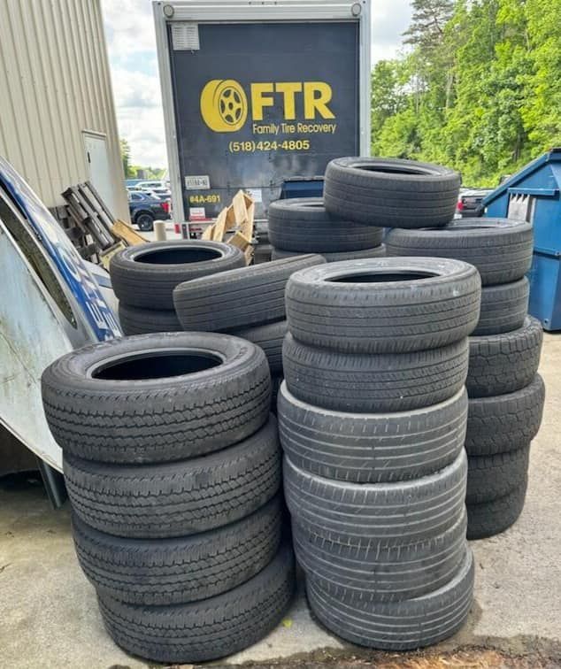 Pile of used tires stacked outdoors in front of a truck with 
