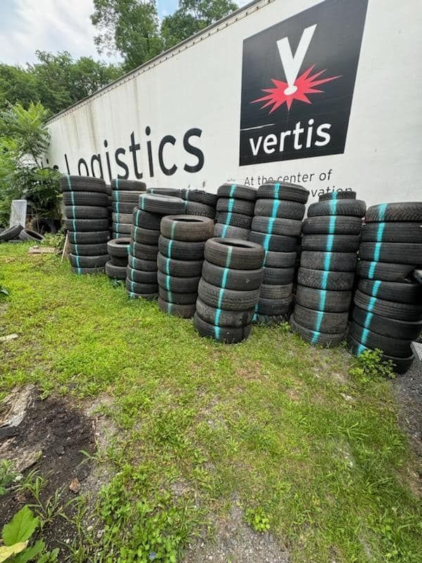 Stacks of tires bundled with teal straps sit on grass in front of a logistics building.