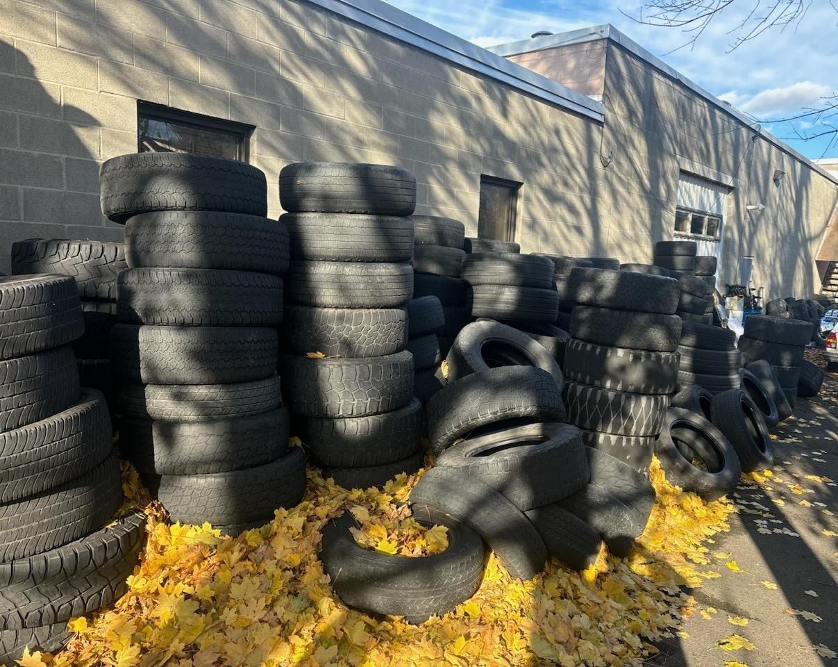 Piles of black tires stacked outside a building with yellow leaves on the ground.