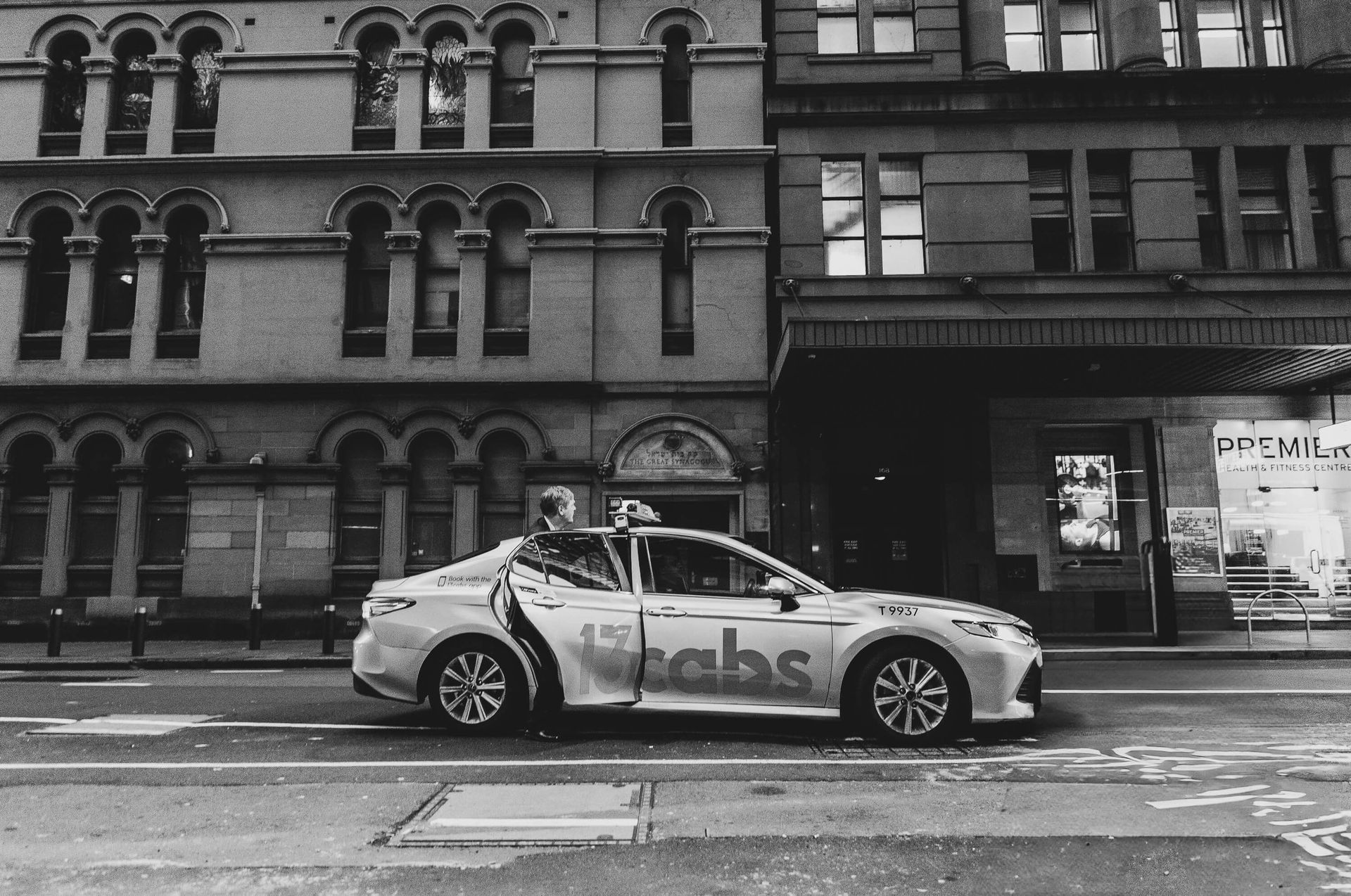 A black and white photo of a 12 cabs car parked in front of a tall building.