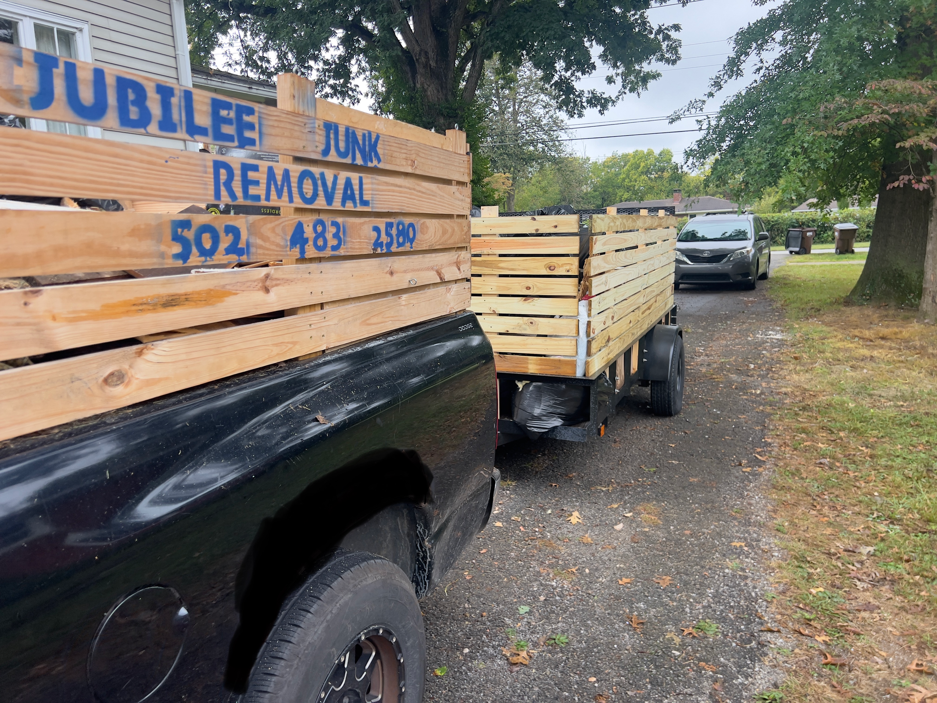 Truck and trailer loaded with wooden debris for jubilee junk removal, parked on a gravel roadside.