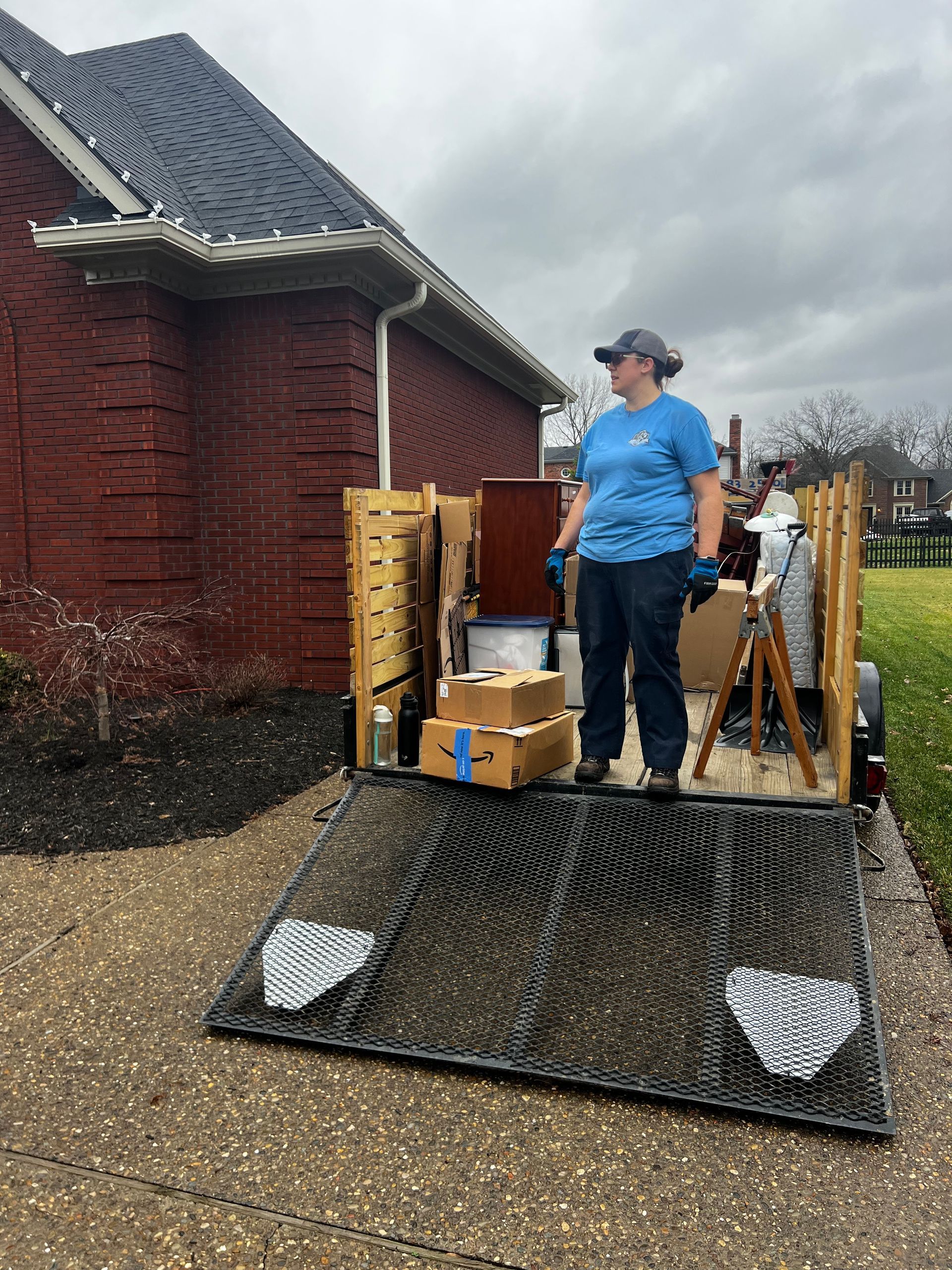Worker standing on a platform beside a brick house, with tools and fencing materials around them.