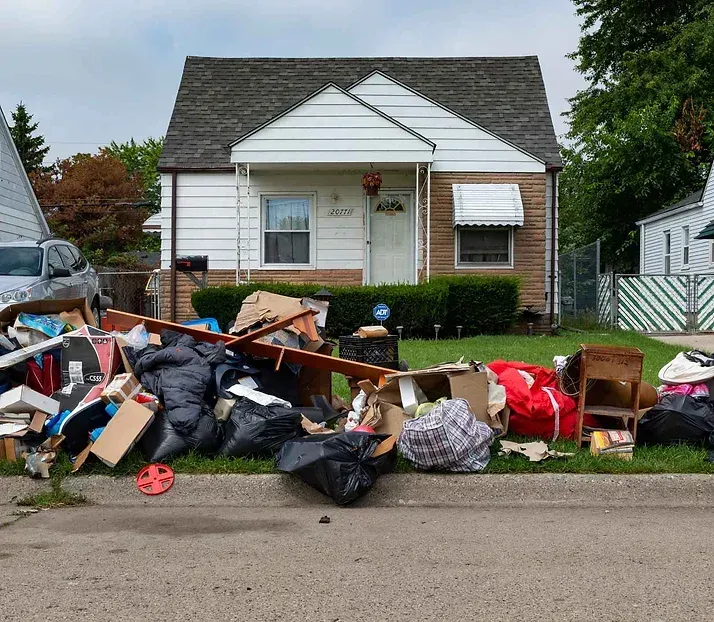 Front yard piled with trash and debris in front of a small white house