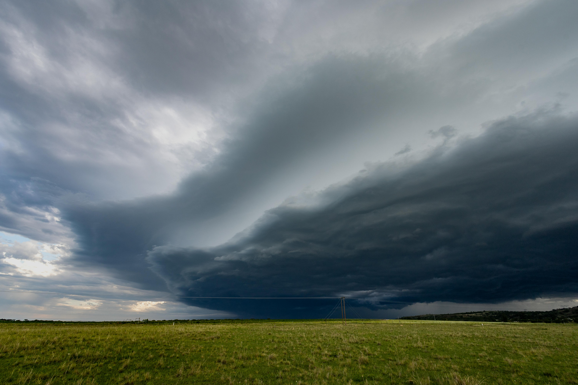 Dark storm clouds over a flat green field and distant horizon