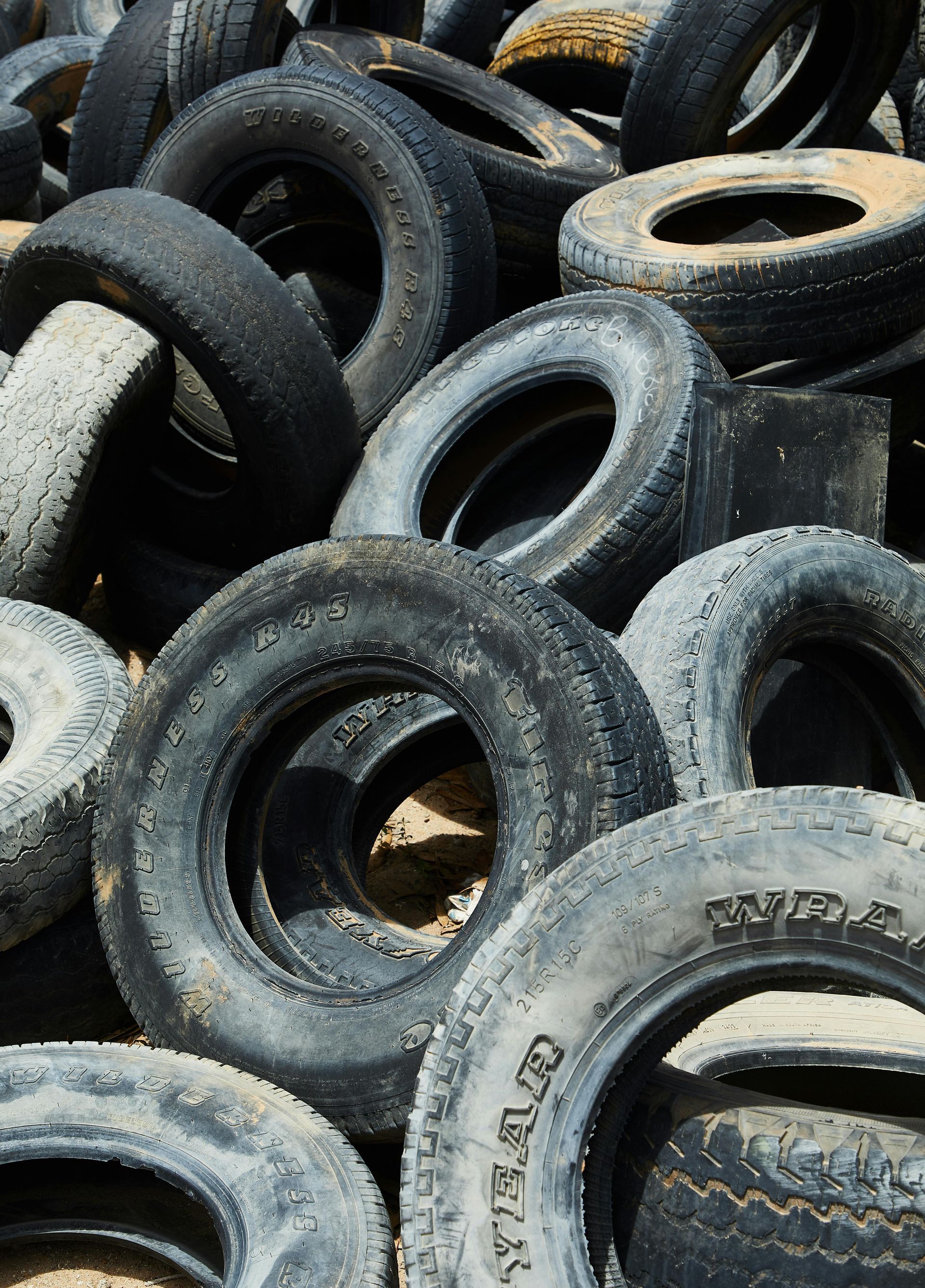 Pile of used tires stacked outdoors, showing worn black rubber and some white-walled tires
