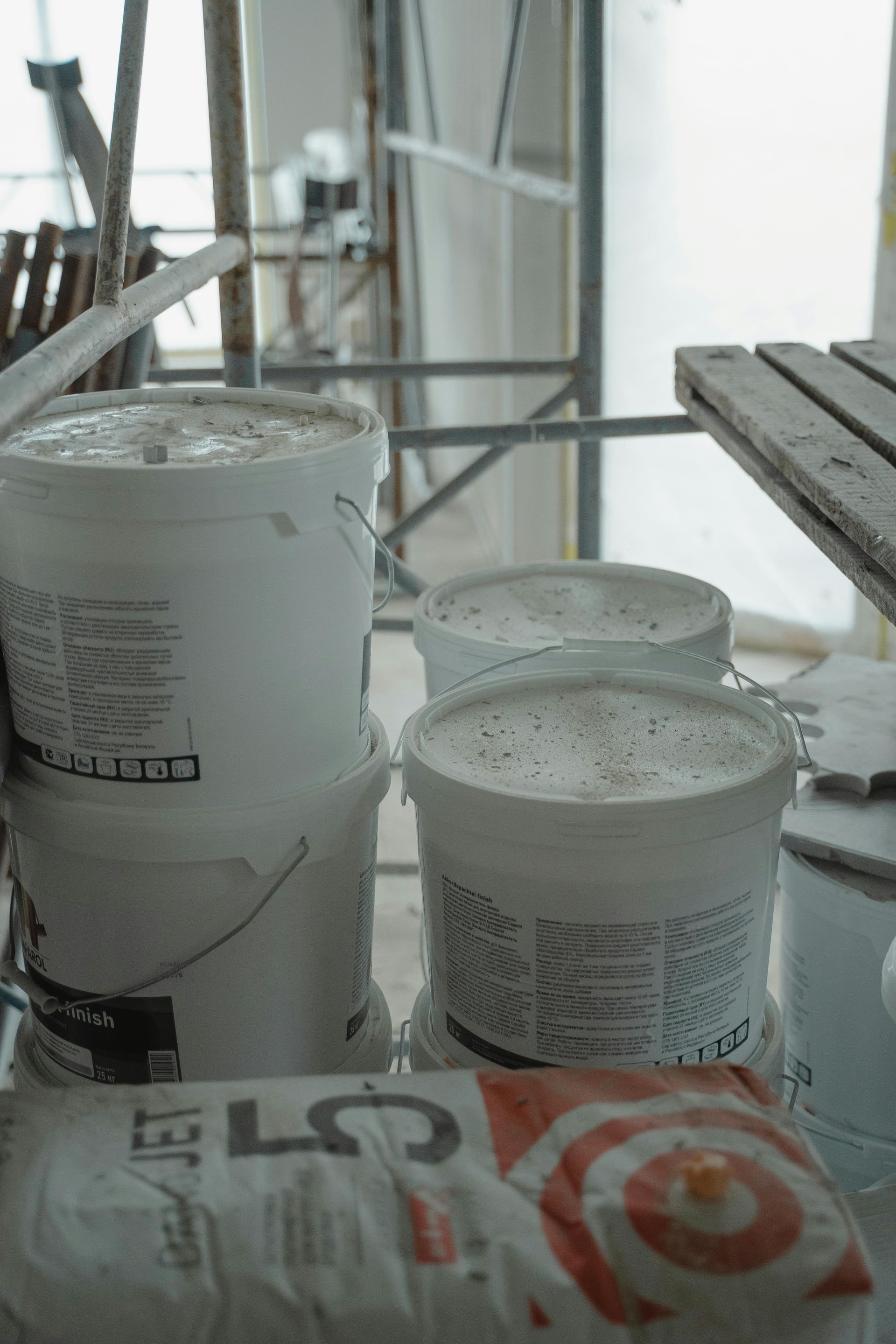 Buckets and paint cans on a scaffold platform at a construction site.