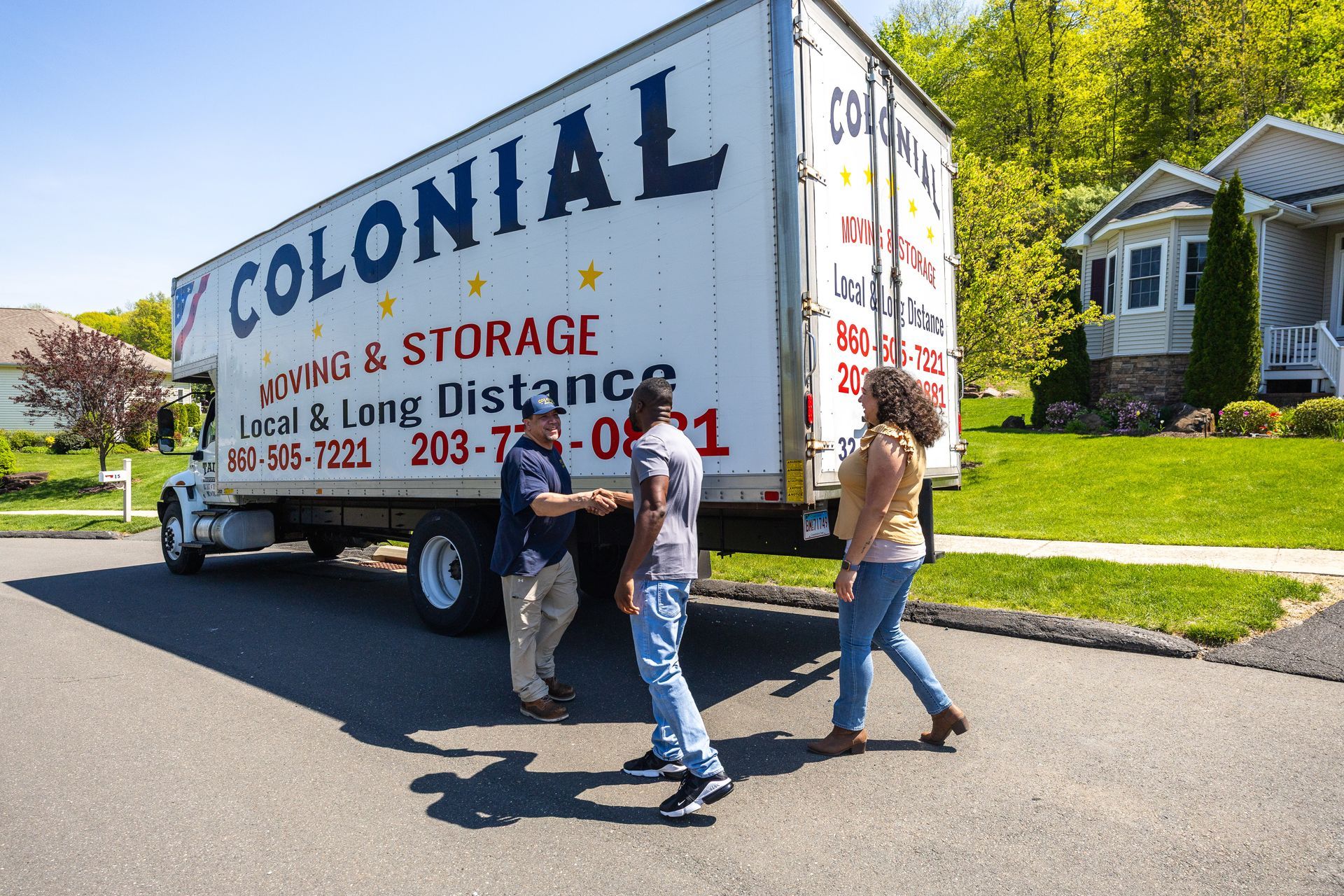 Moving truck for Colonial Moving & Storage with two people walking beside it on a sunny street