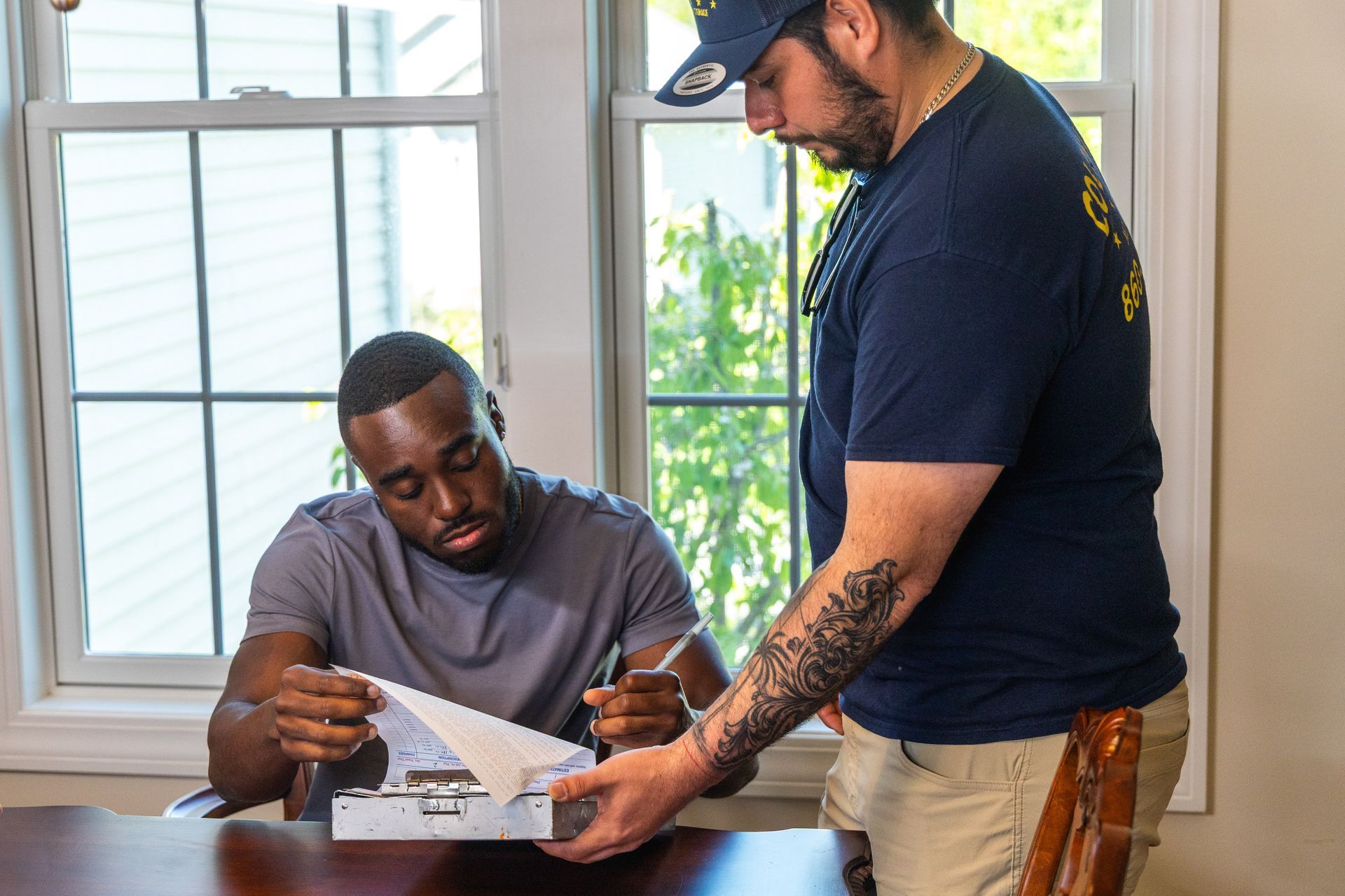 Two men reviewing paperwork at a table by a bright window