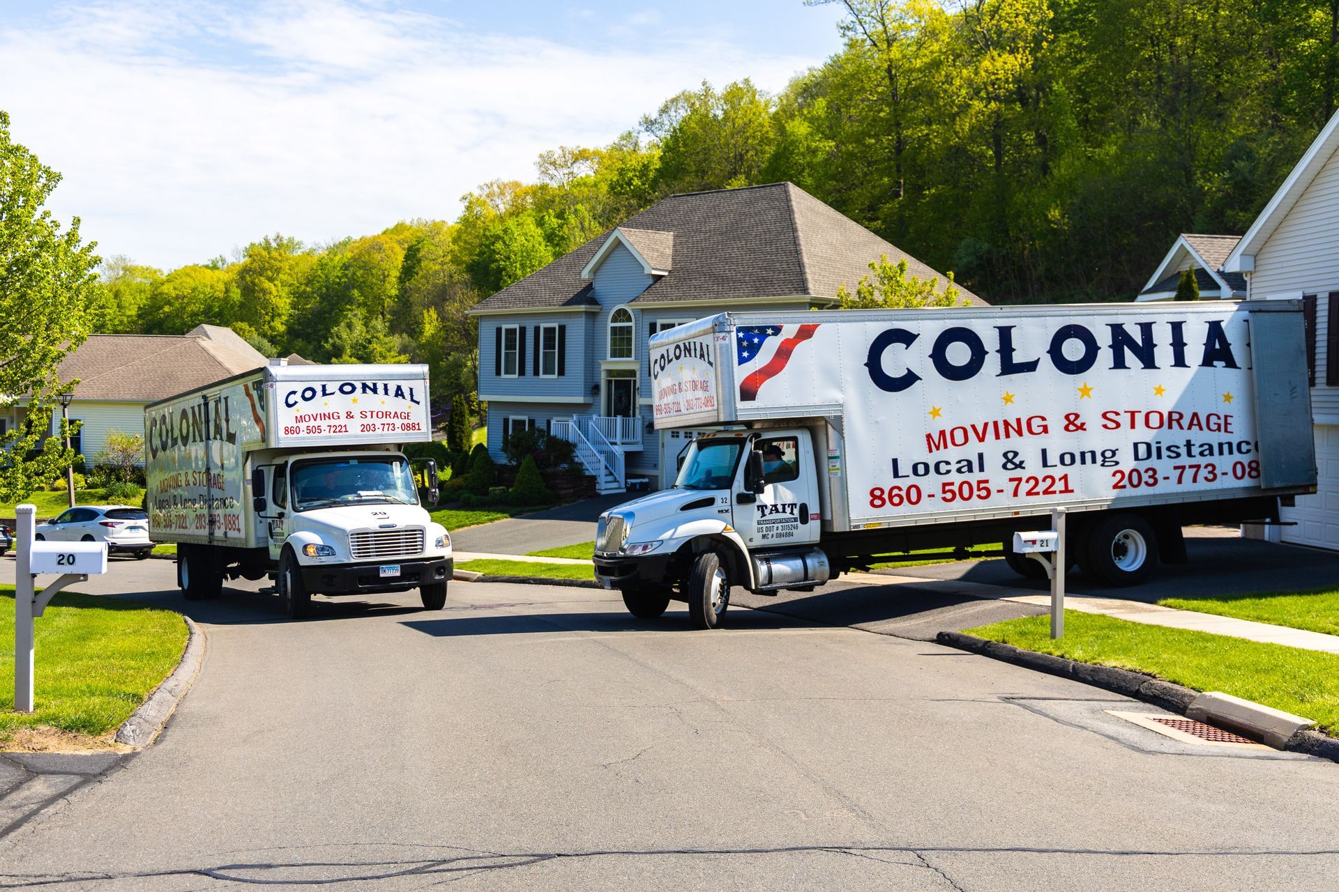 Two Colonial Moving & Storage trucks parked on a suburban street lined with trees and houses