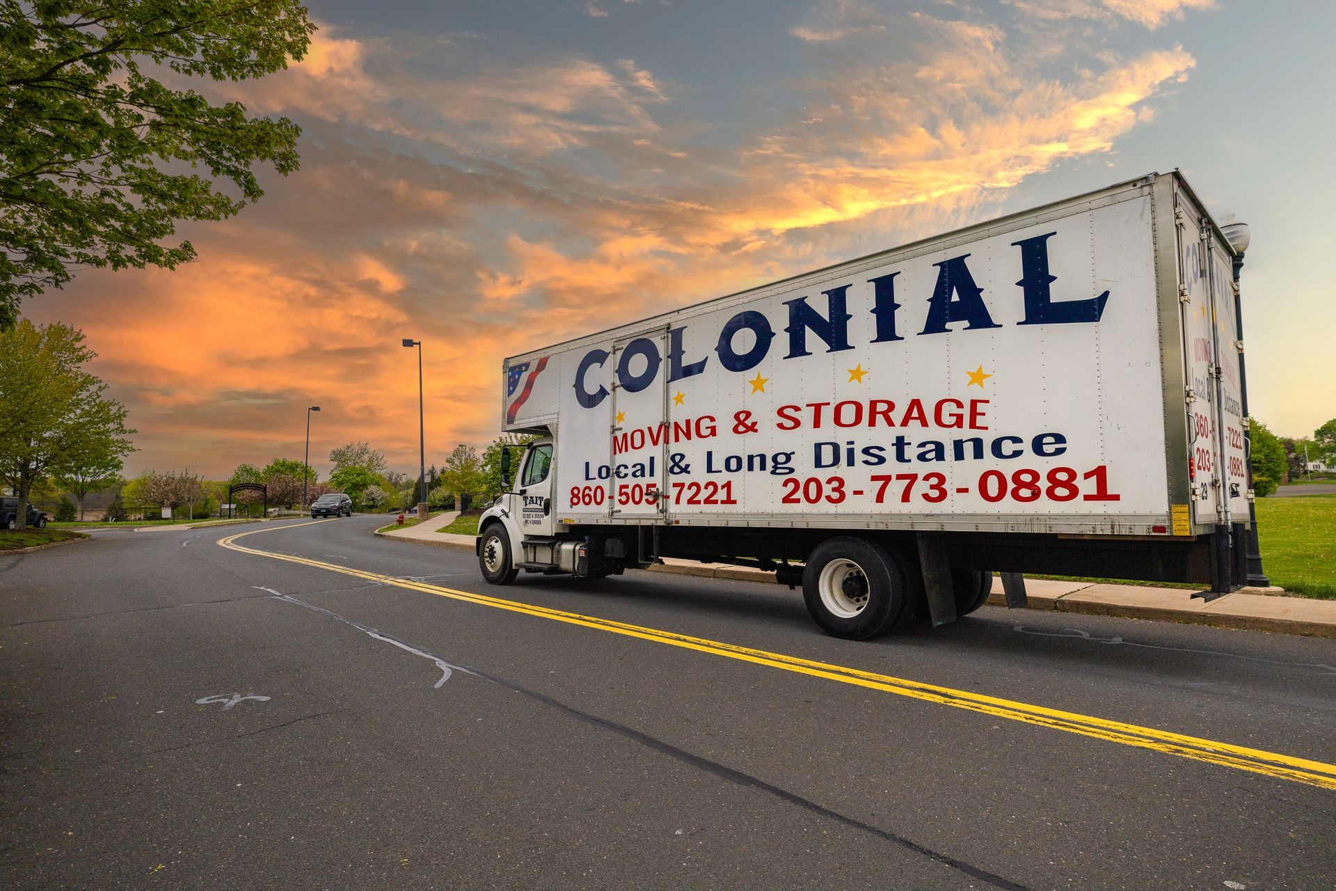 Moving truck with Colonial Moving & Storage branding parked on a road at sunset.