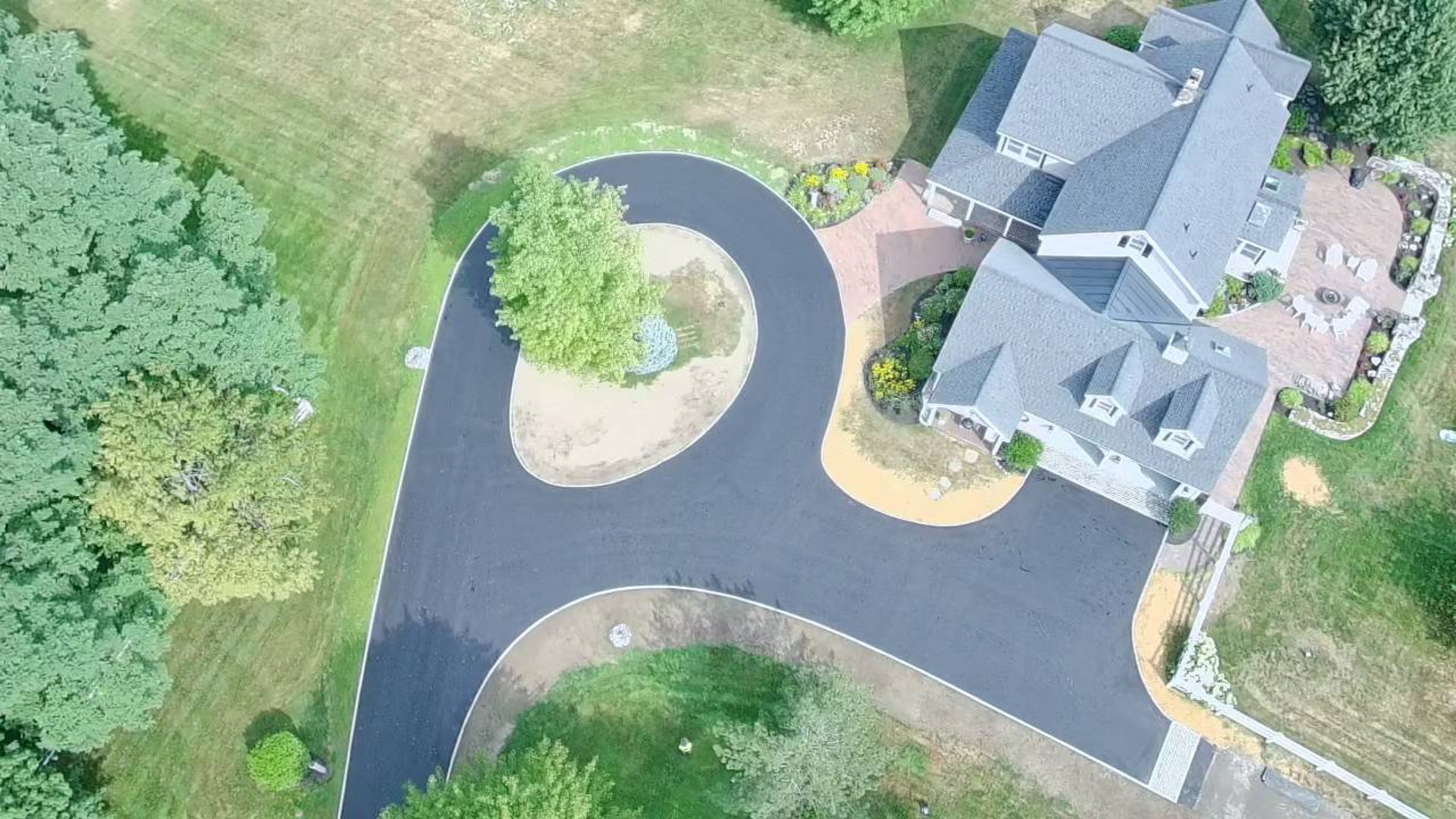 Brick house with a dark garage door, driveway, and green lawn and shrubs.