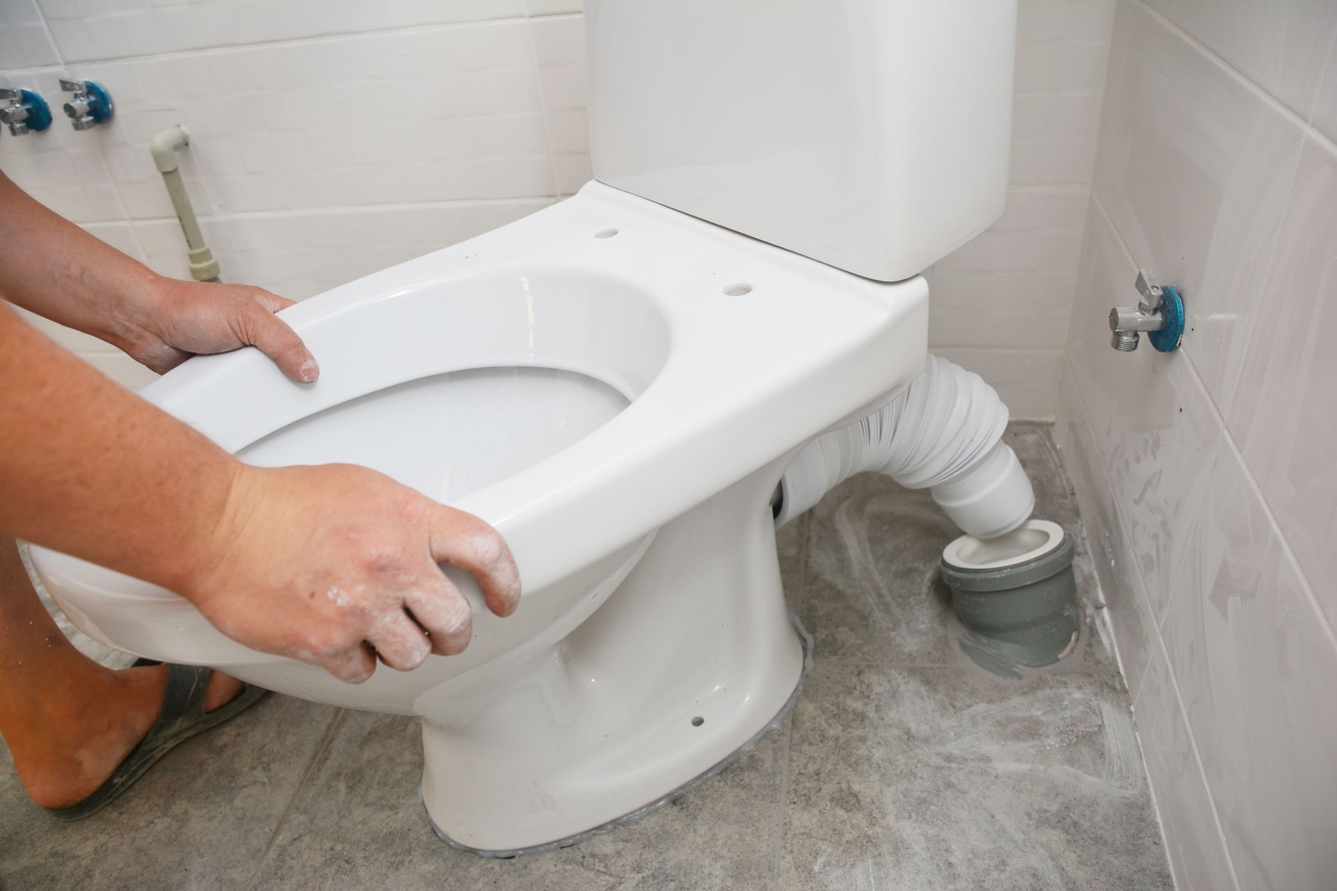 Repairman's hands installing a flush toilet, securing the toilet bowl in the bathroom.