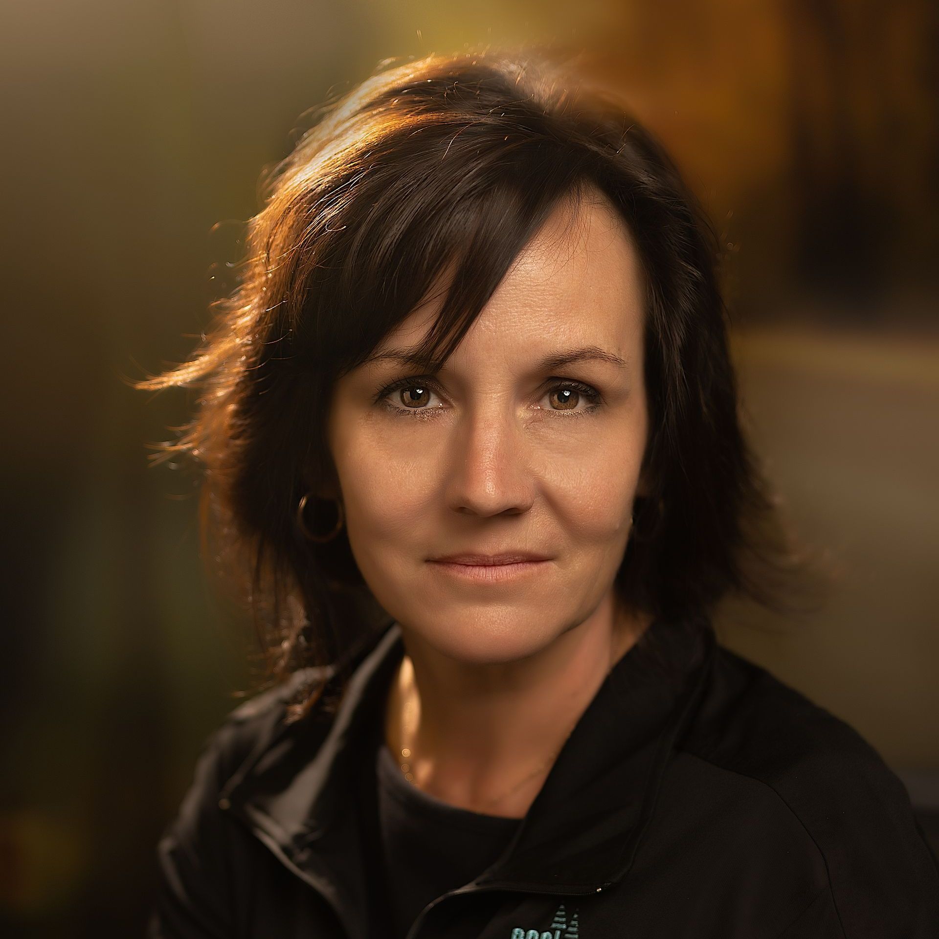 Portrait of a woman with dark hair in a black jacket against a blurred warm background