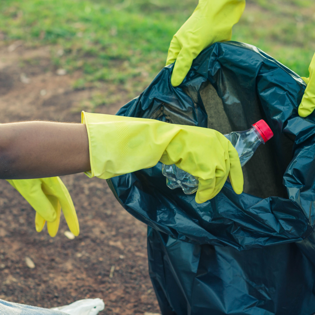 Gloved hands placing trash into a black garbage bag outdoors