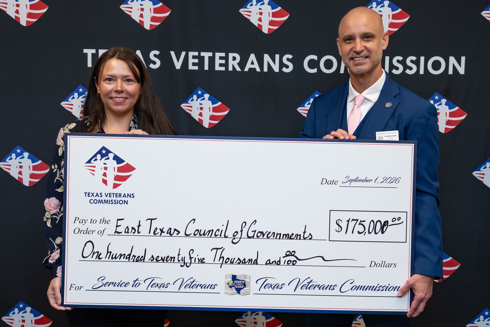Two people hold a large ceremonial check in front of a Texas Veterans Commission backdrop.