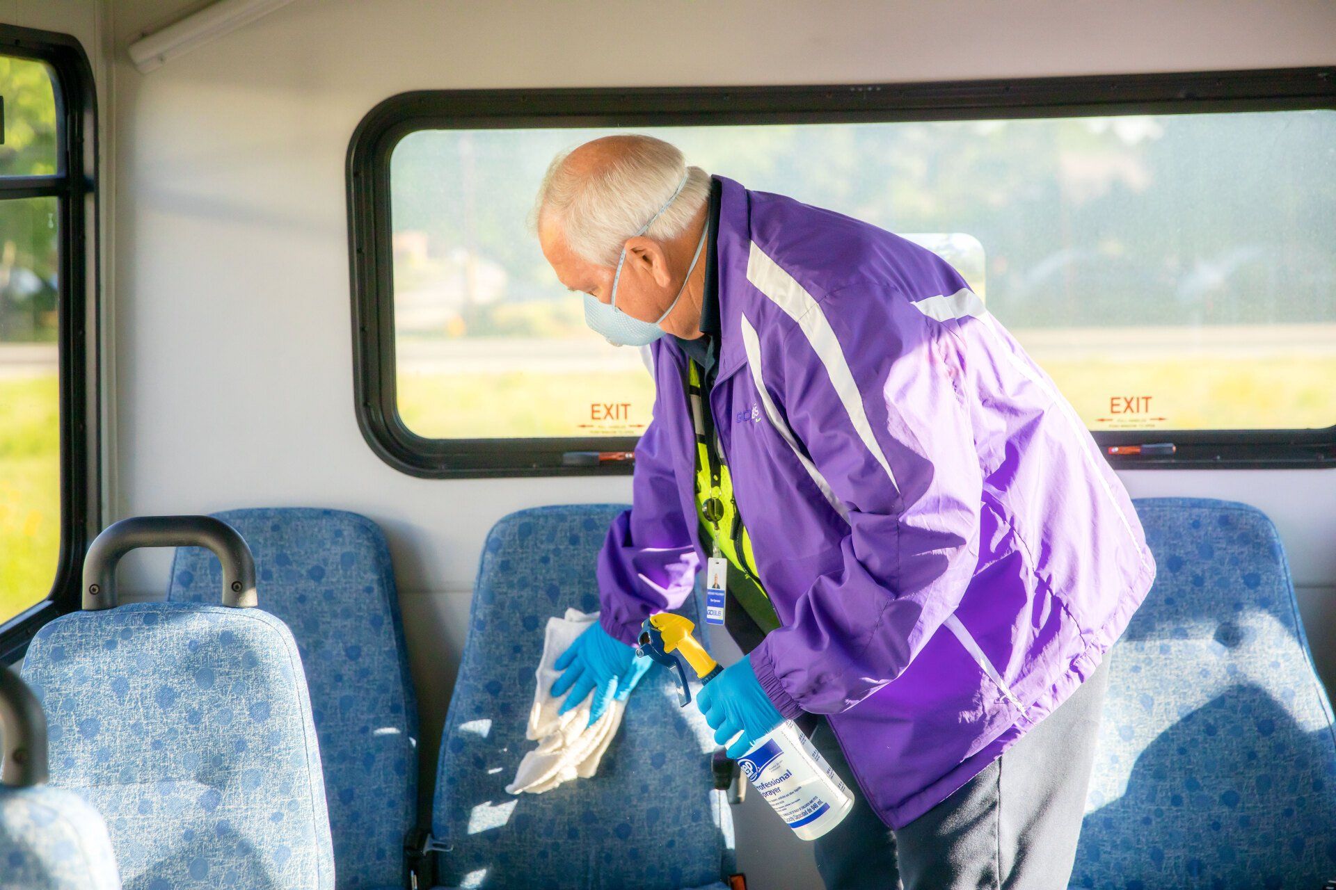 A man wearing a mask is cleaning the seats of a bus.