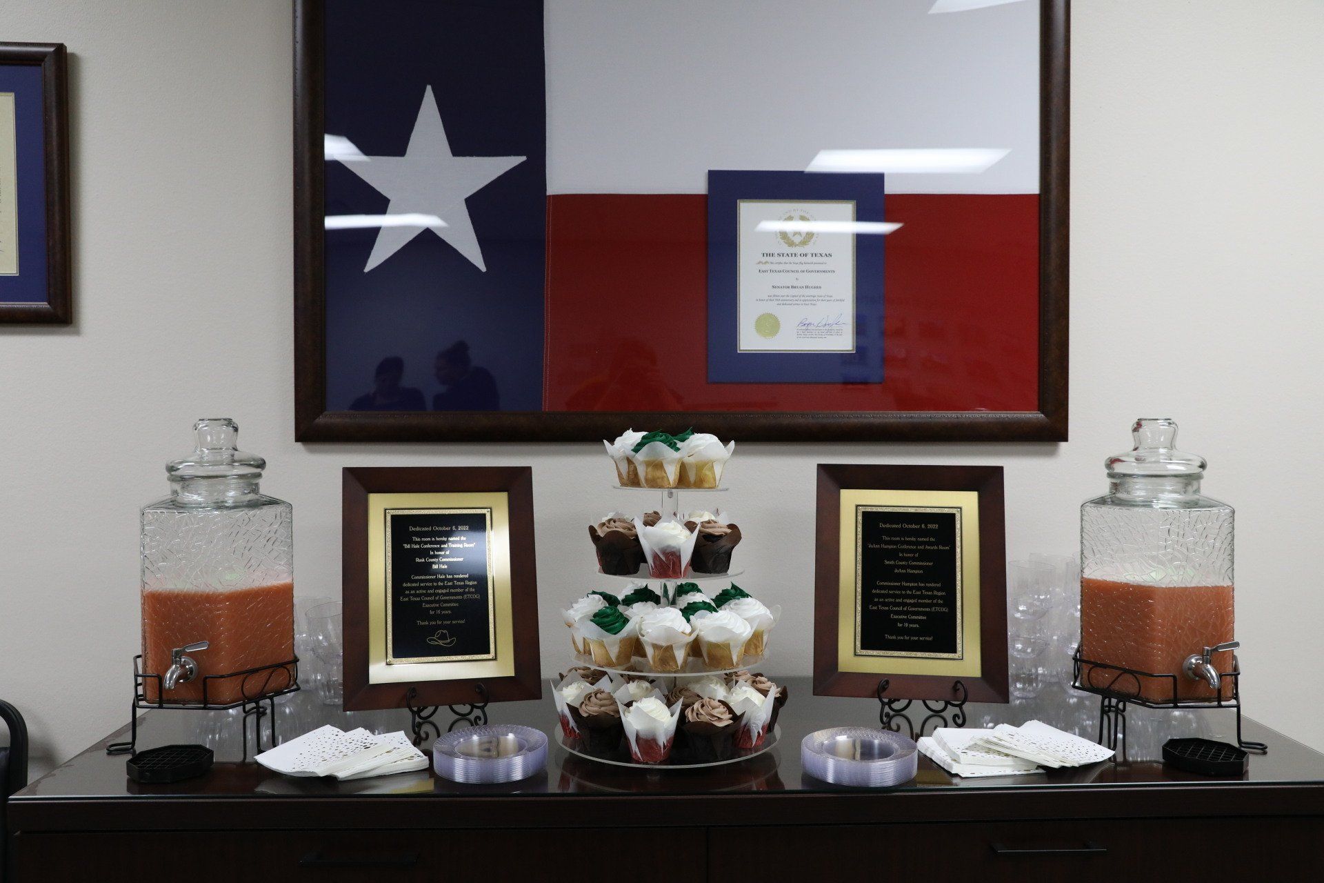 A table with cupcakes and drinks in front of a texas flag