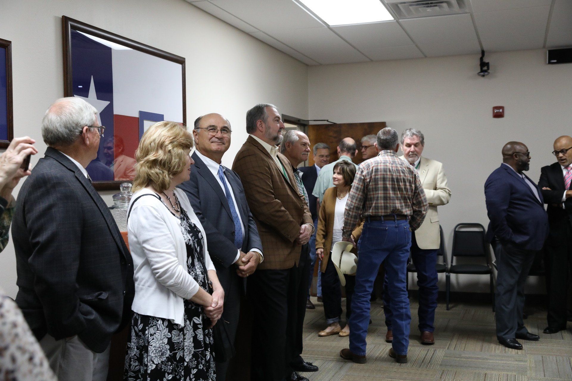 A group of people are standing in a room with a texas flag on the wall.