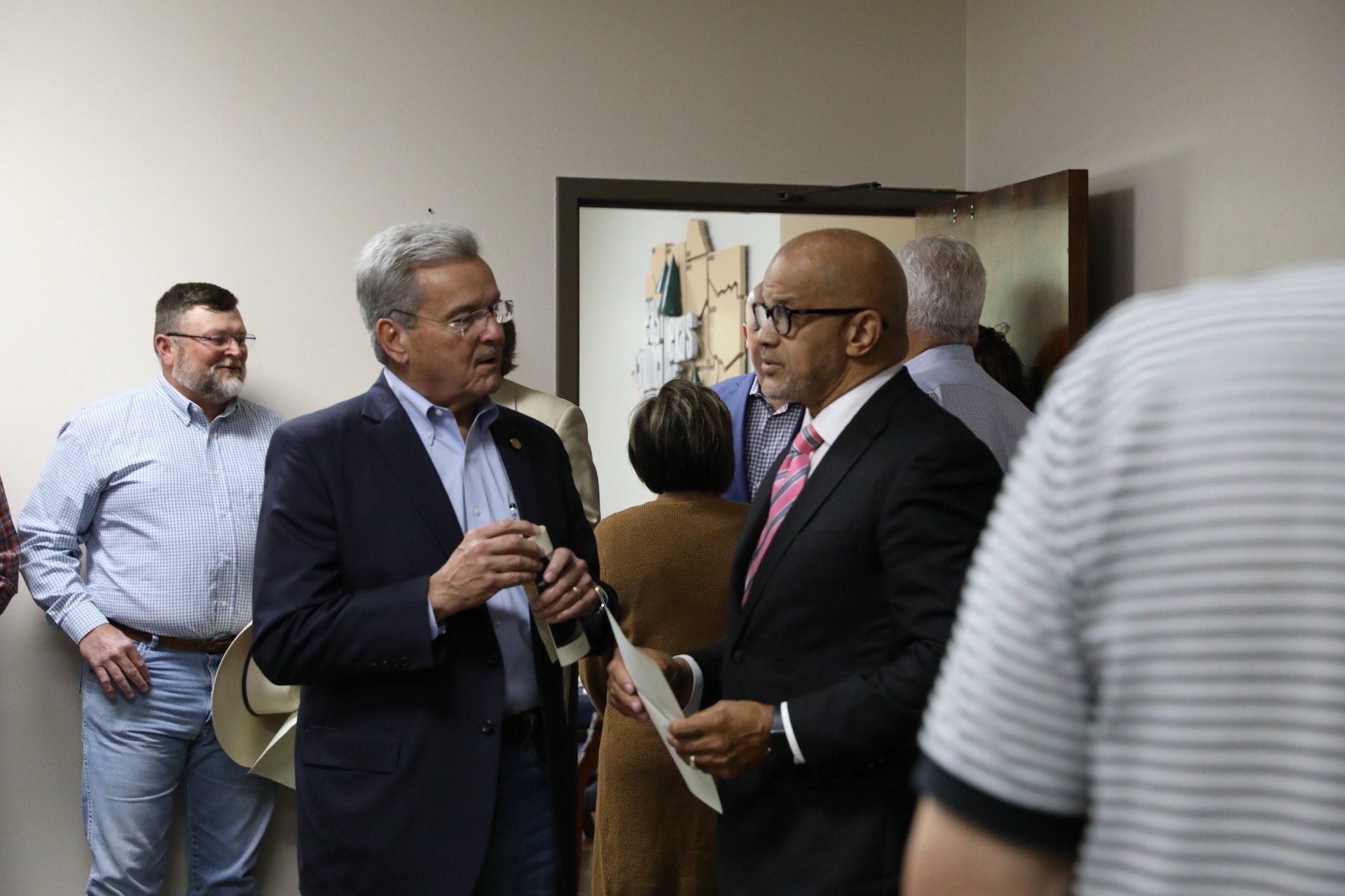 A group of men are standing in a room talking to each other.