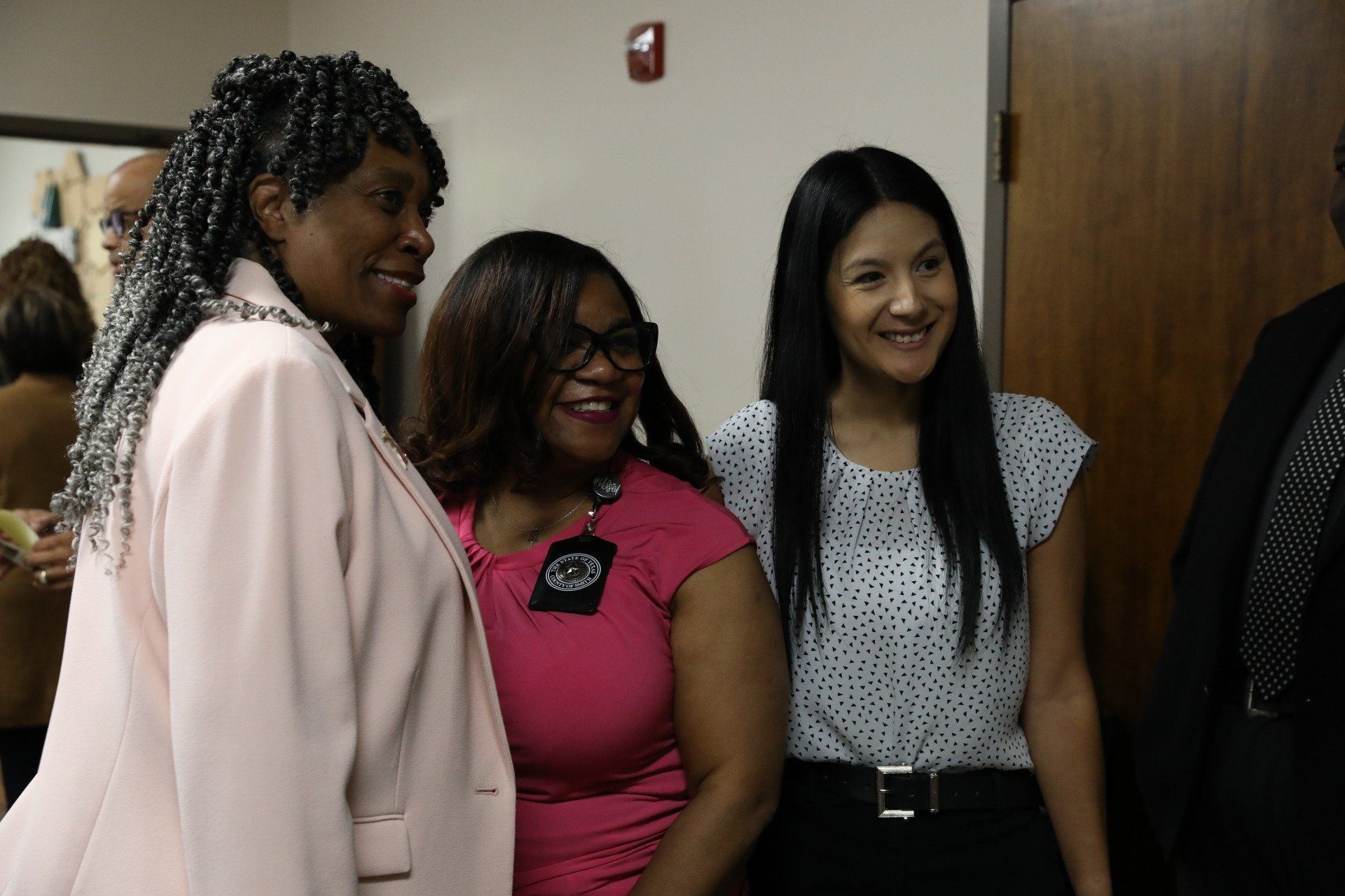 Three women are standing next to each other in a room and smiling.