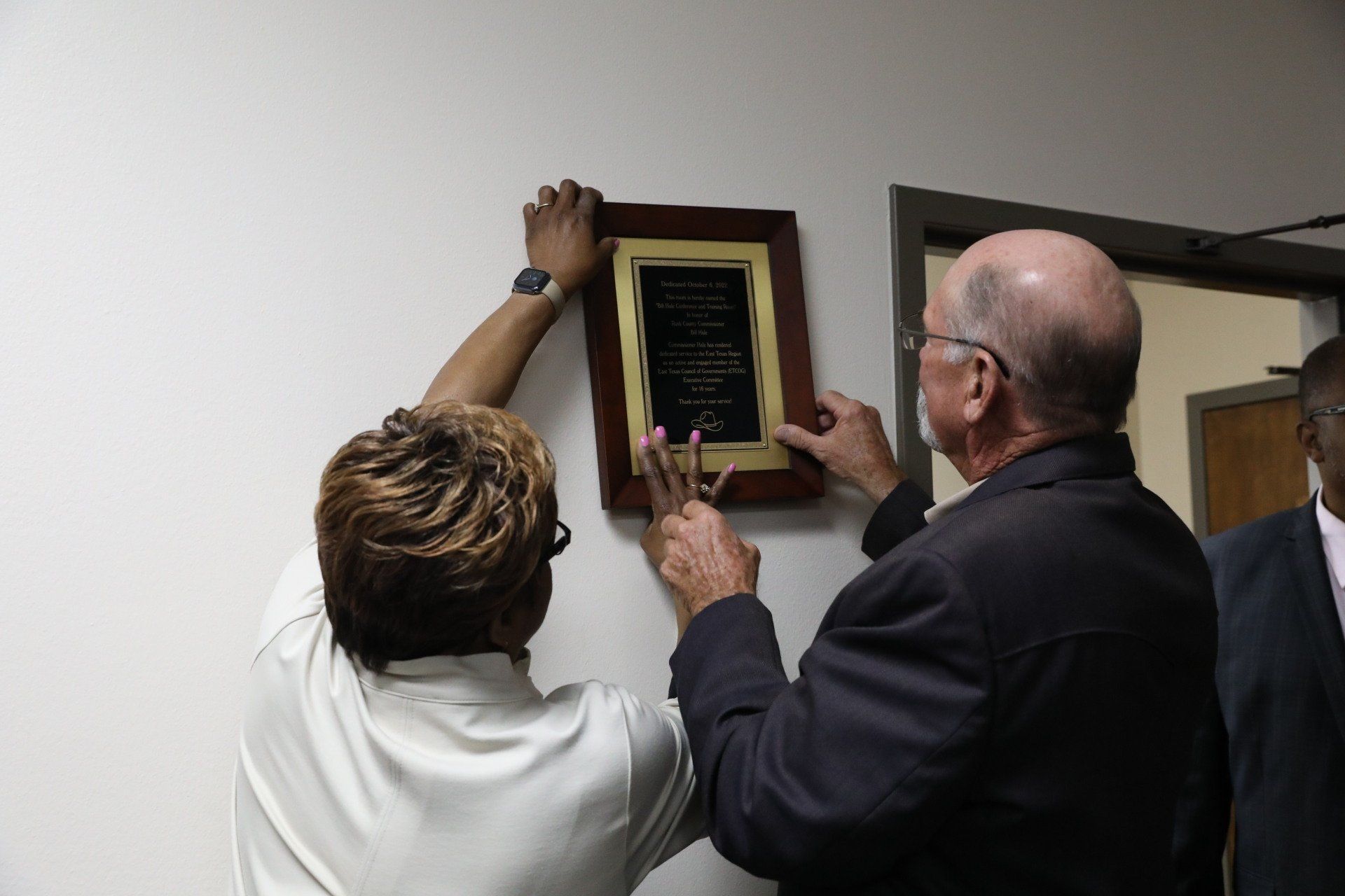 A man and a woman are hanging a plaque on a wall.