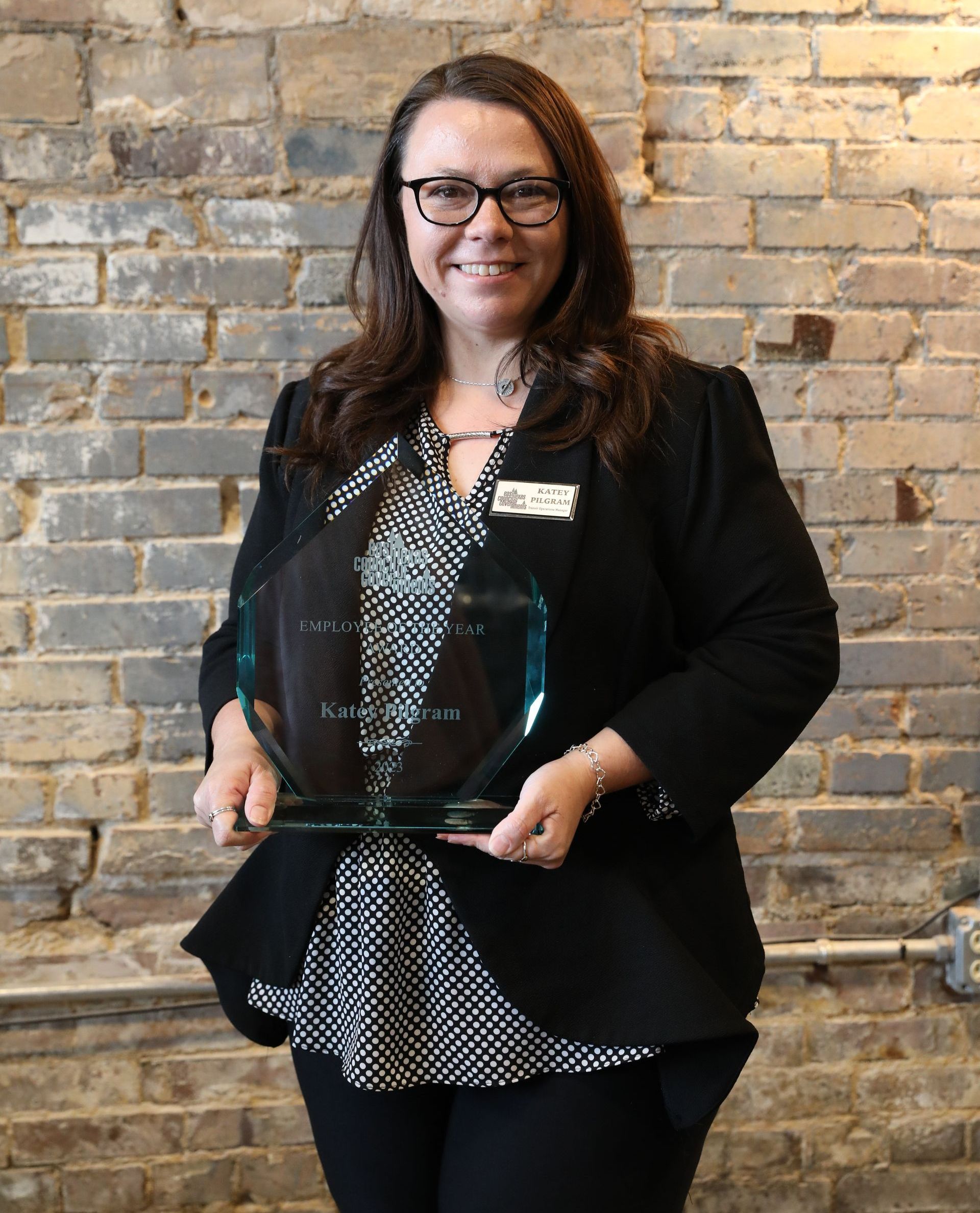 A woman is holding a trophy in front of a brick wall.