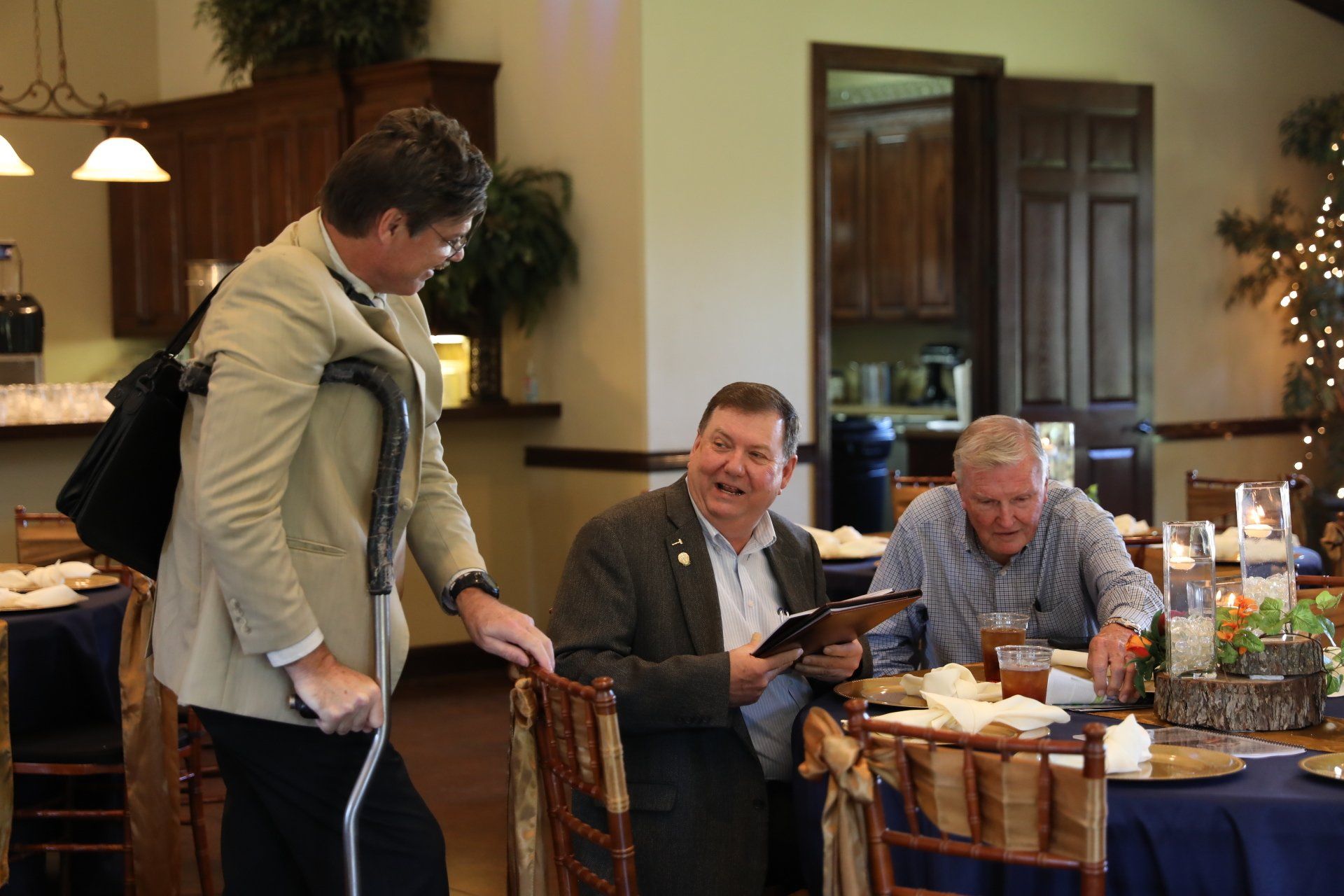 A man with a cane is standing next to a group of men sitting at tables.